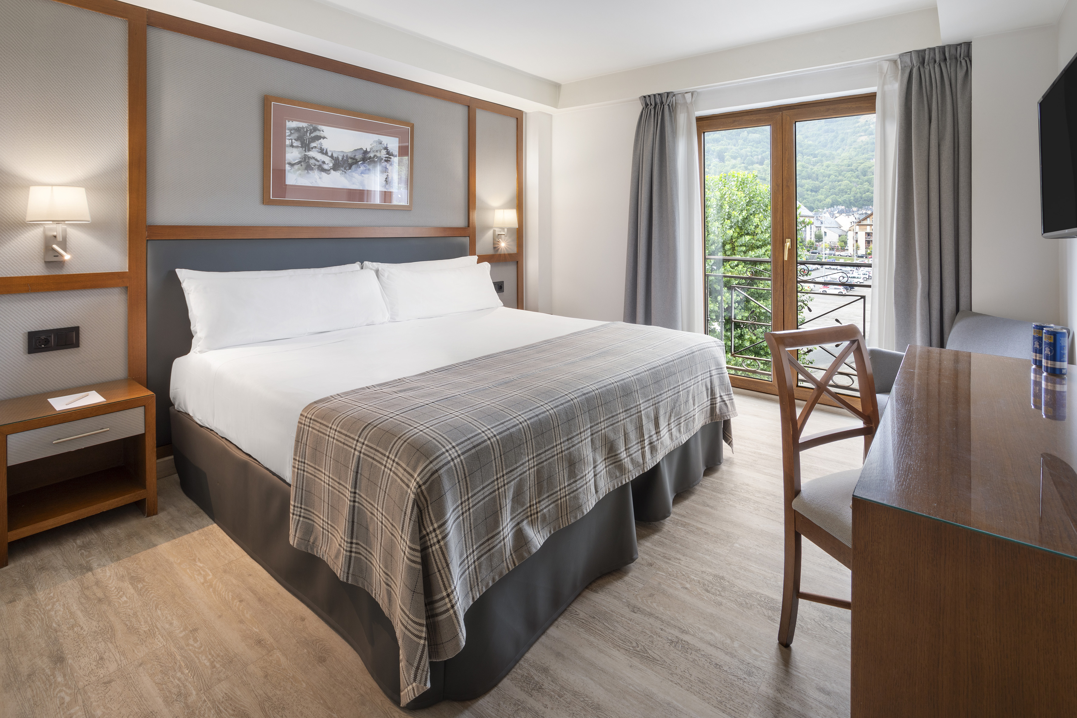 Habitación de hotel con cama doble, balcón con vista a la montaña y escritorio.