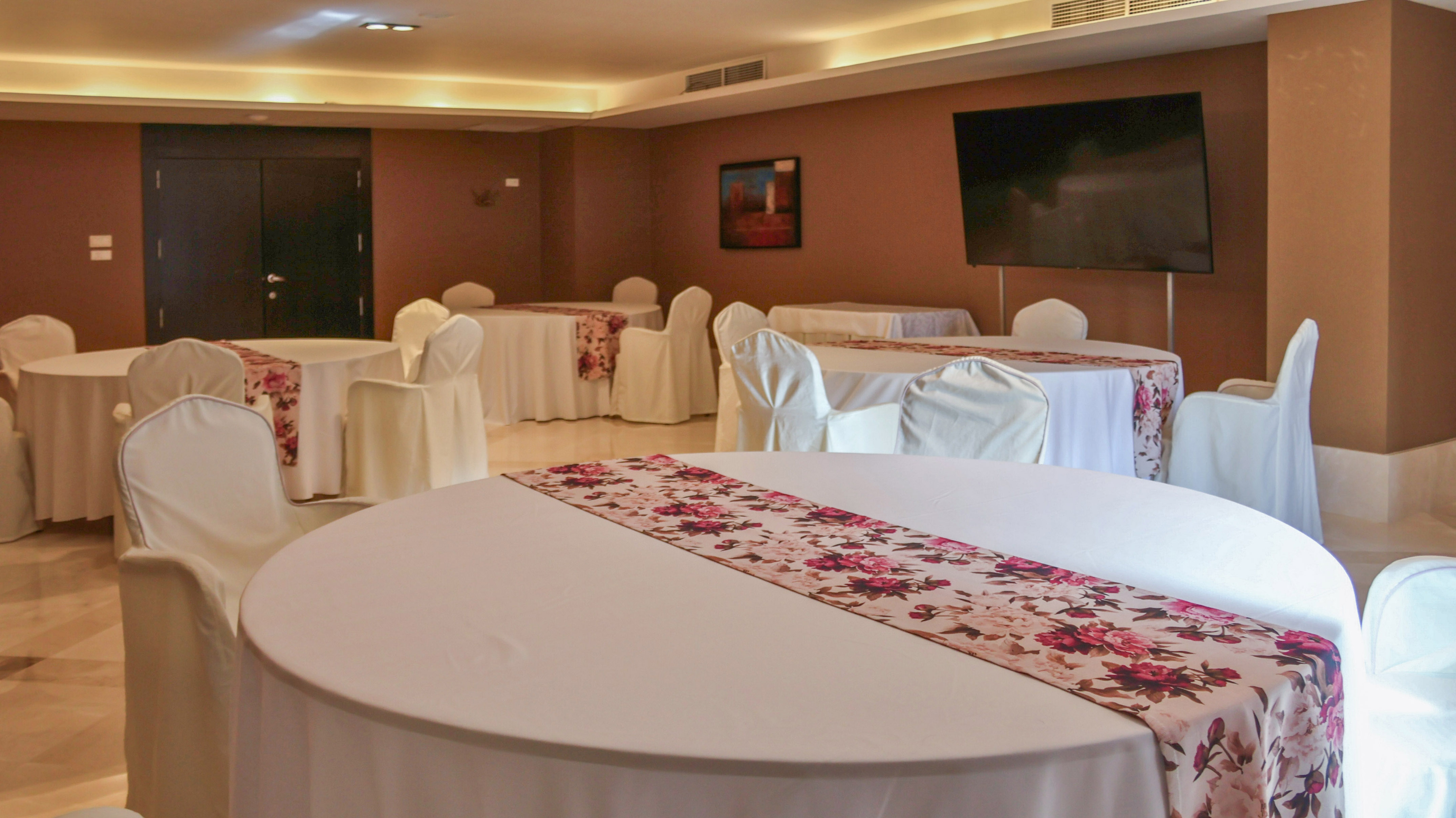 Banquet hall with round tables, white covers, and pink floral runners.