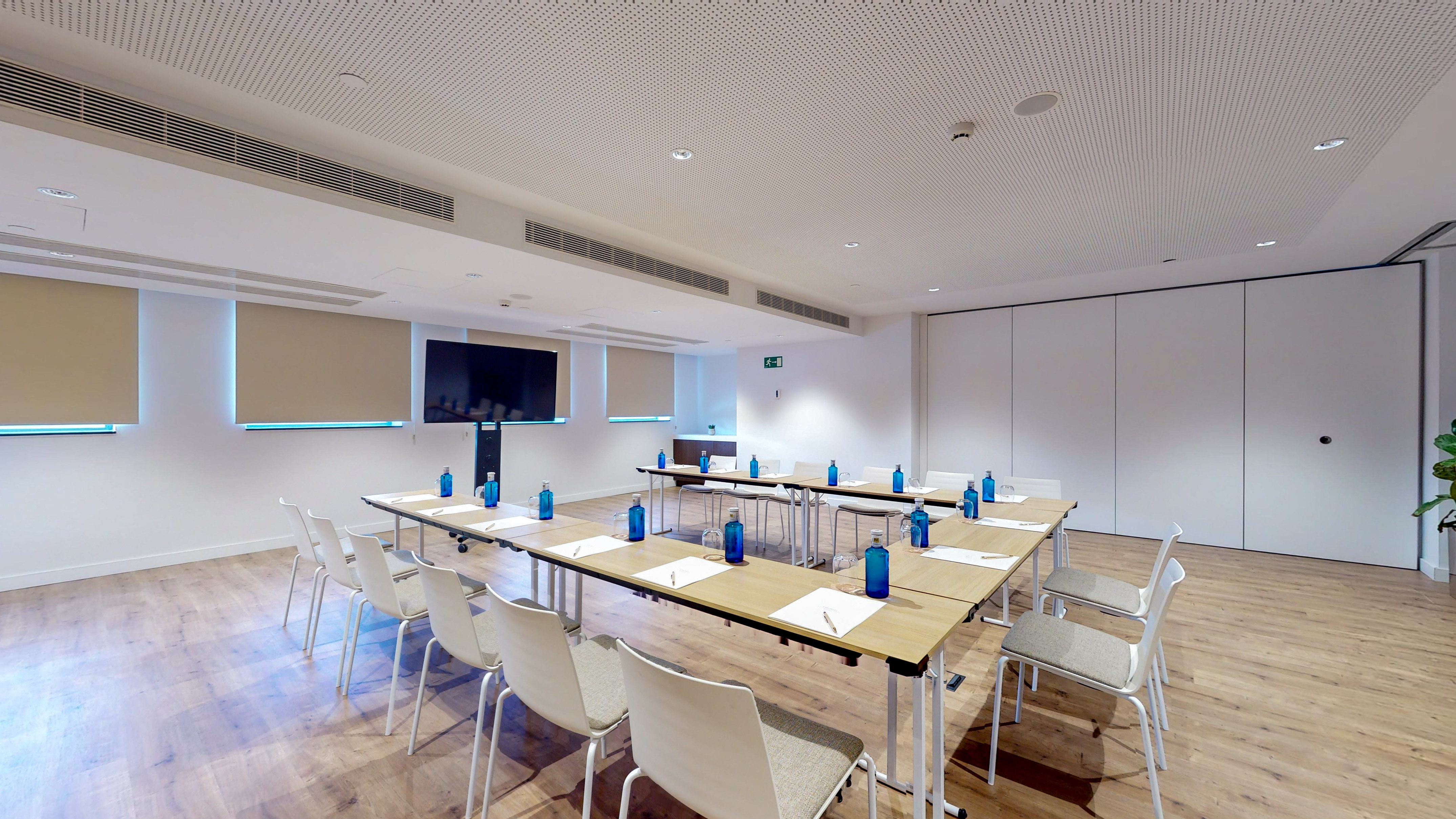 Modern U-shaped conference room with tables, chairs, and large screen.