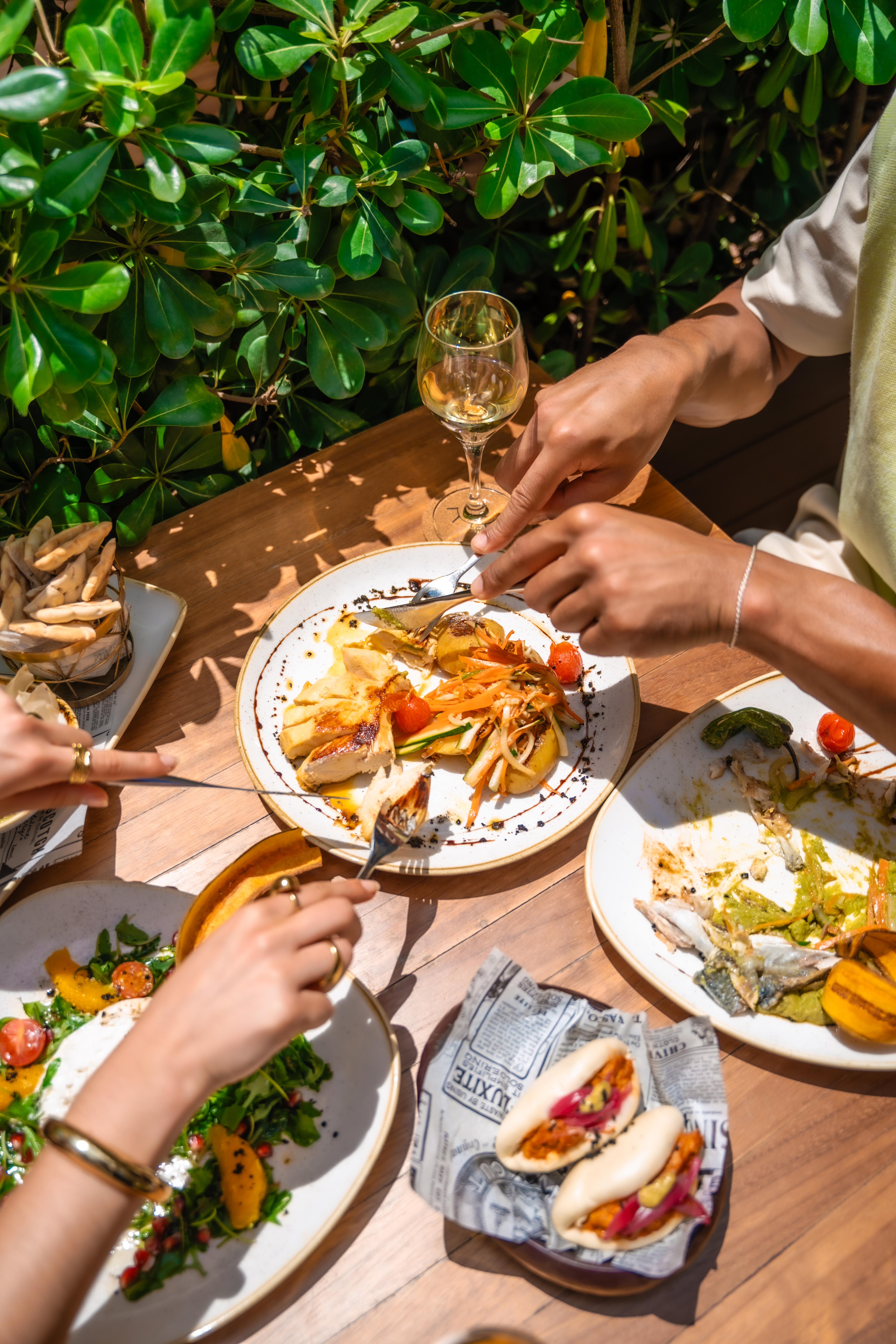 Outdoor restaurant meal with chicken, salad, bao buns, and white wine.