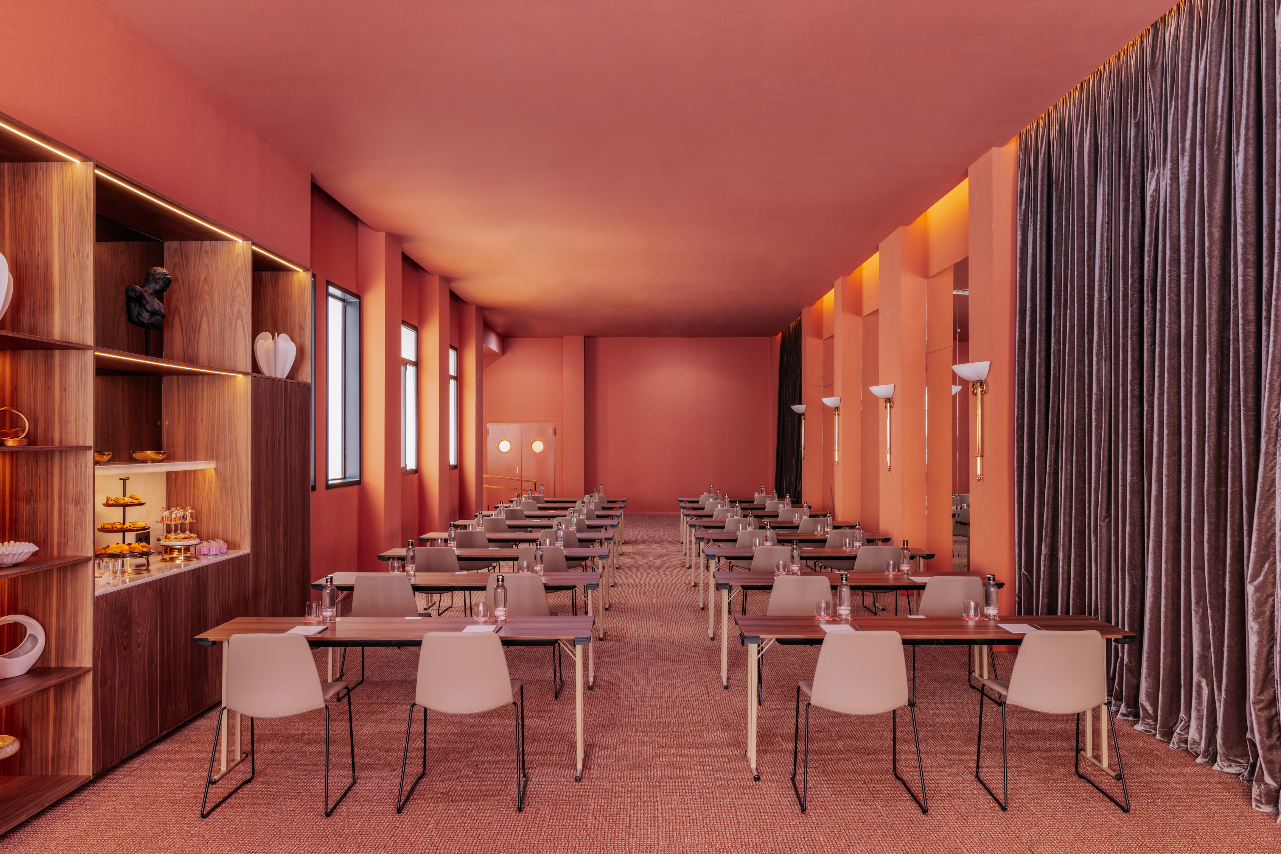 Terracotta meeting room with rows of tables, chairs, and a snack bar.