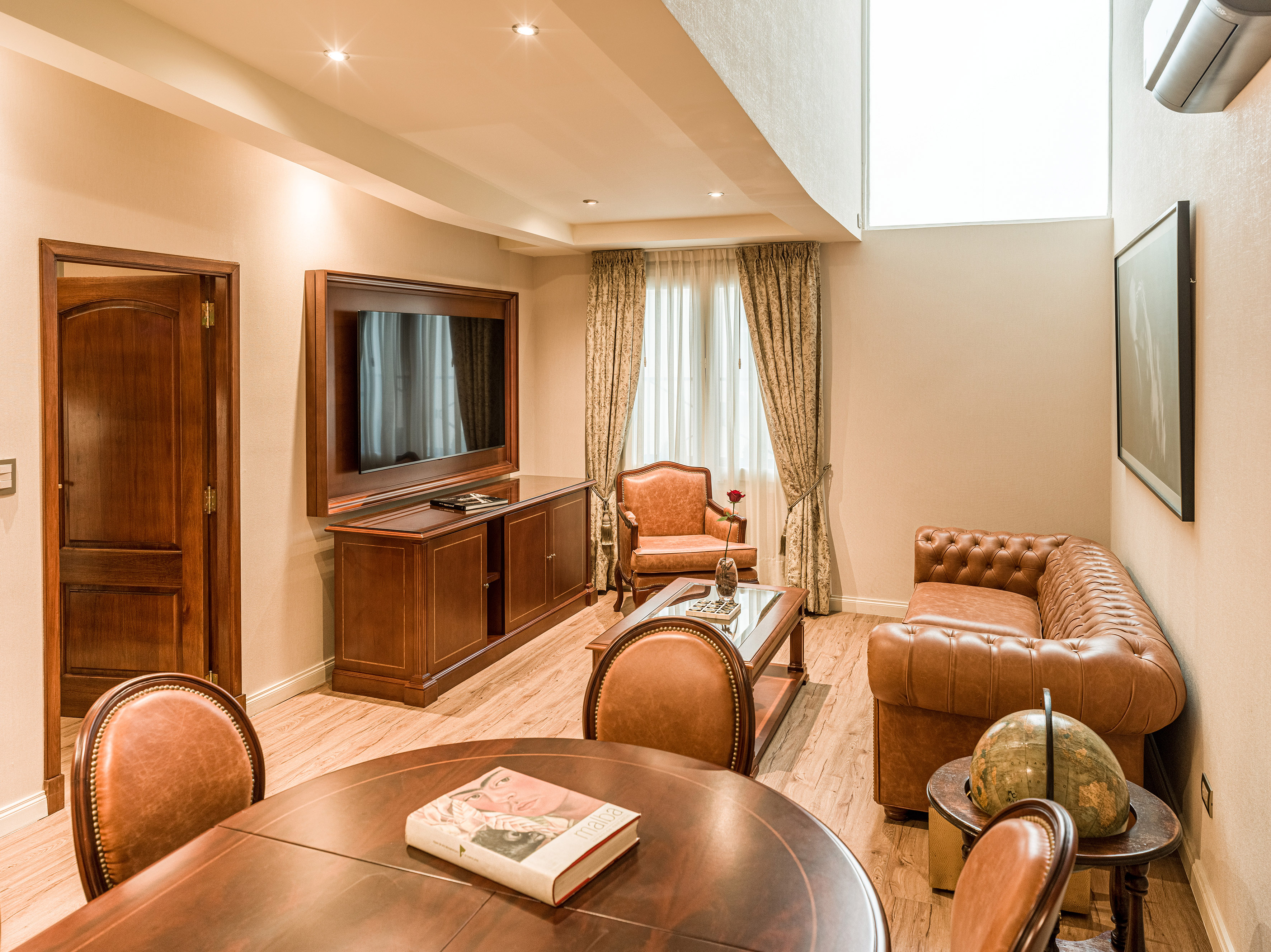 Luxurious hotel suite living room with brown leather furniture and wooden decor.
