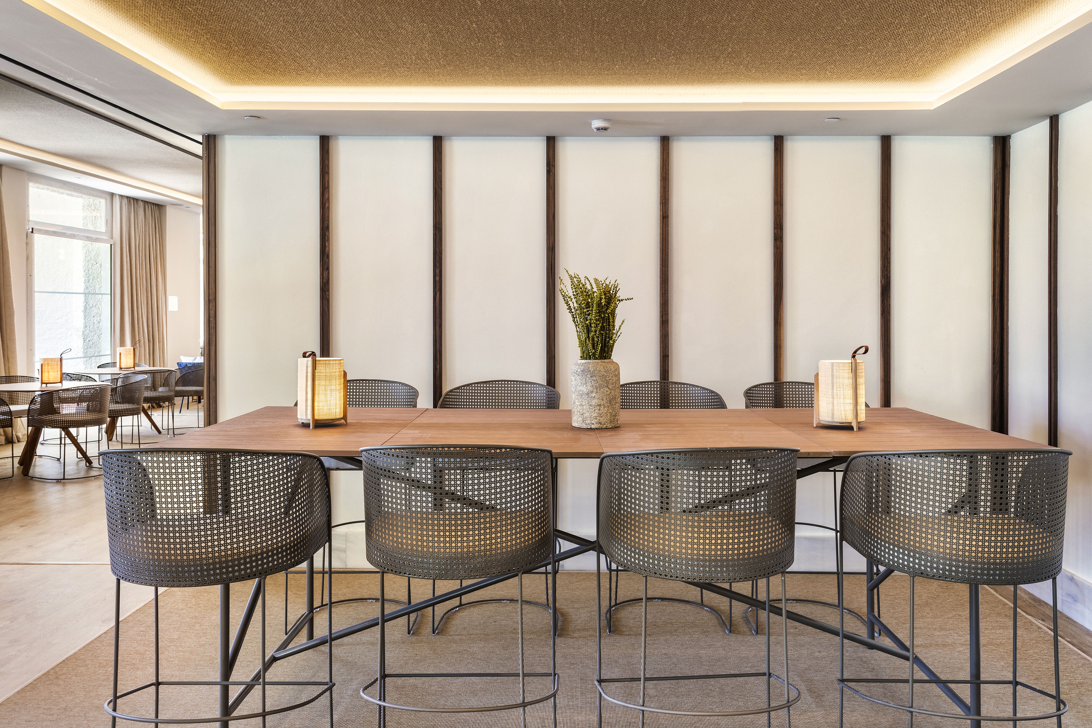 Modern communal table with perforated bar stools and plant. Hotel restaurant.