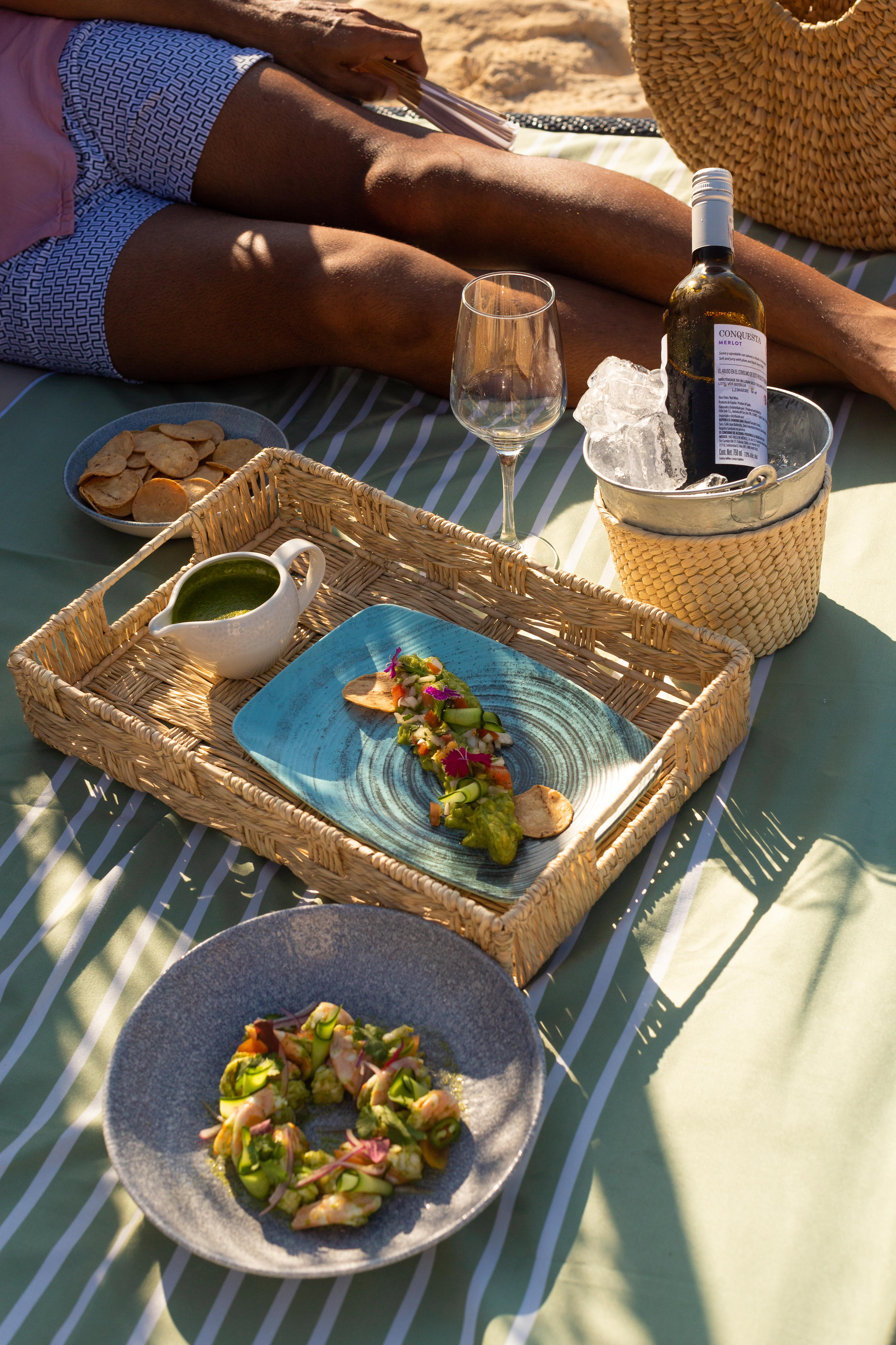 Beach picnic with wine, shrimp and avocado appetizers, person relaxing.