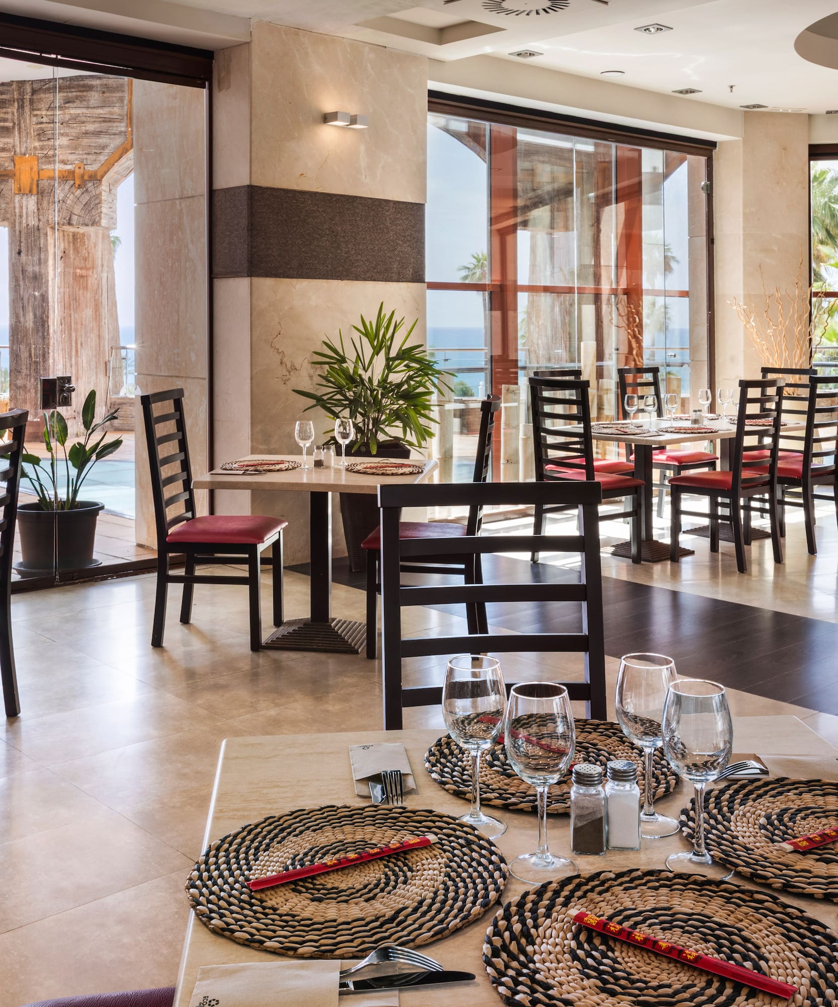 Resort restaurant with ocean view, palm trees, and elegantly set dining tables.