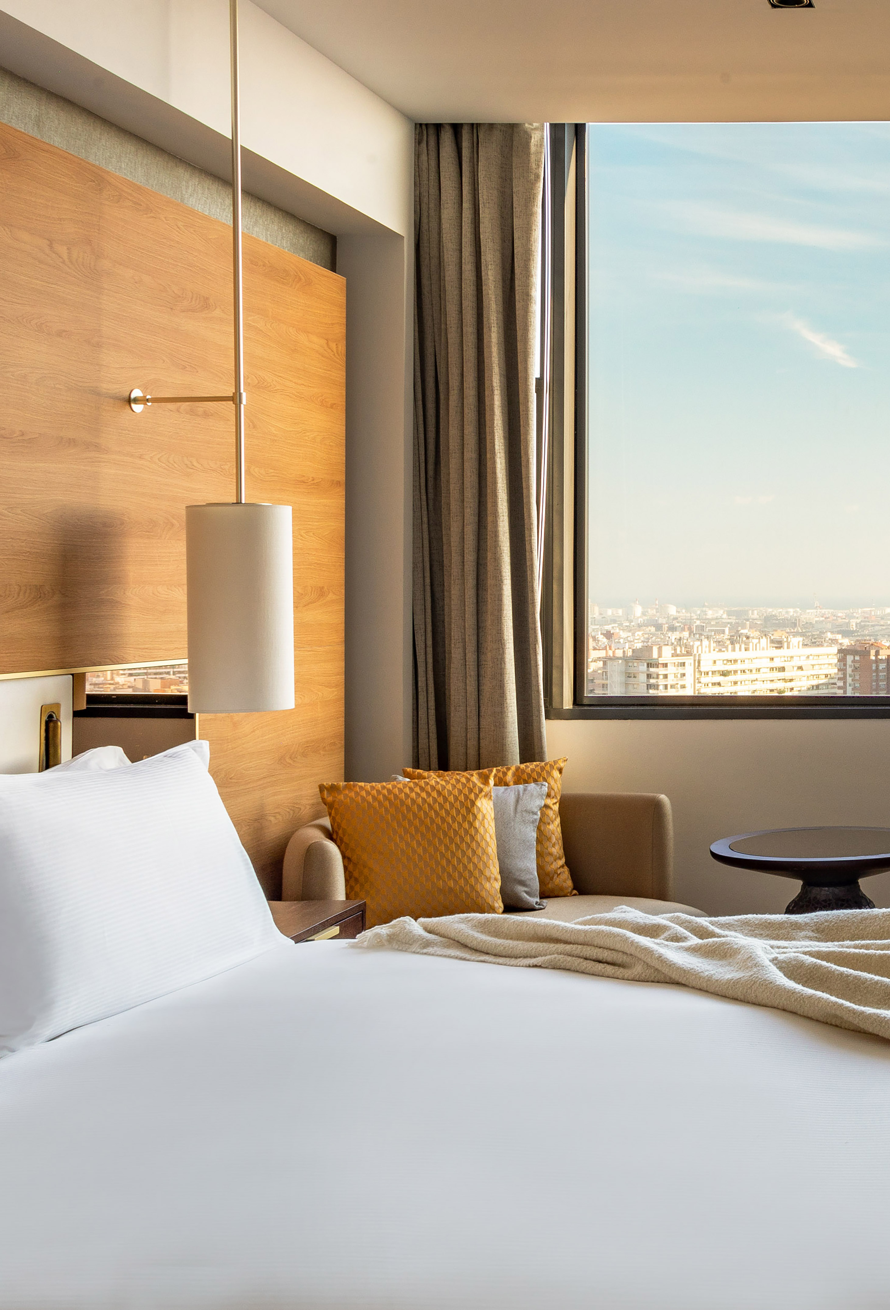 Bright hotel room featuring a bed, wooden paneling, and panoramic city view.