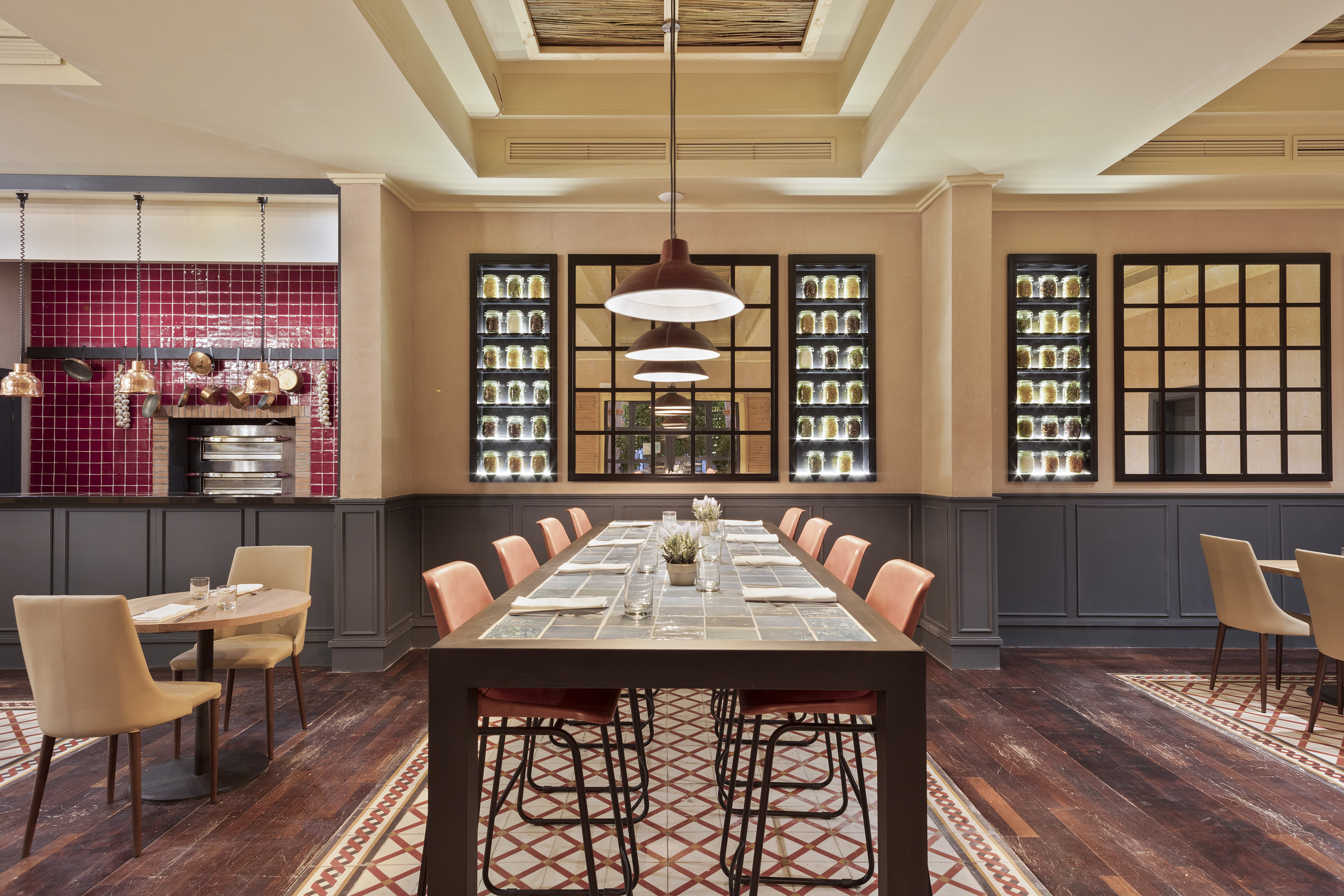 Restaurant dining room with long communal table, red tiled kitchen, and spice jars.