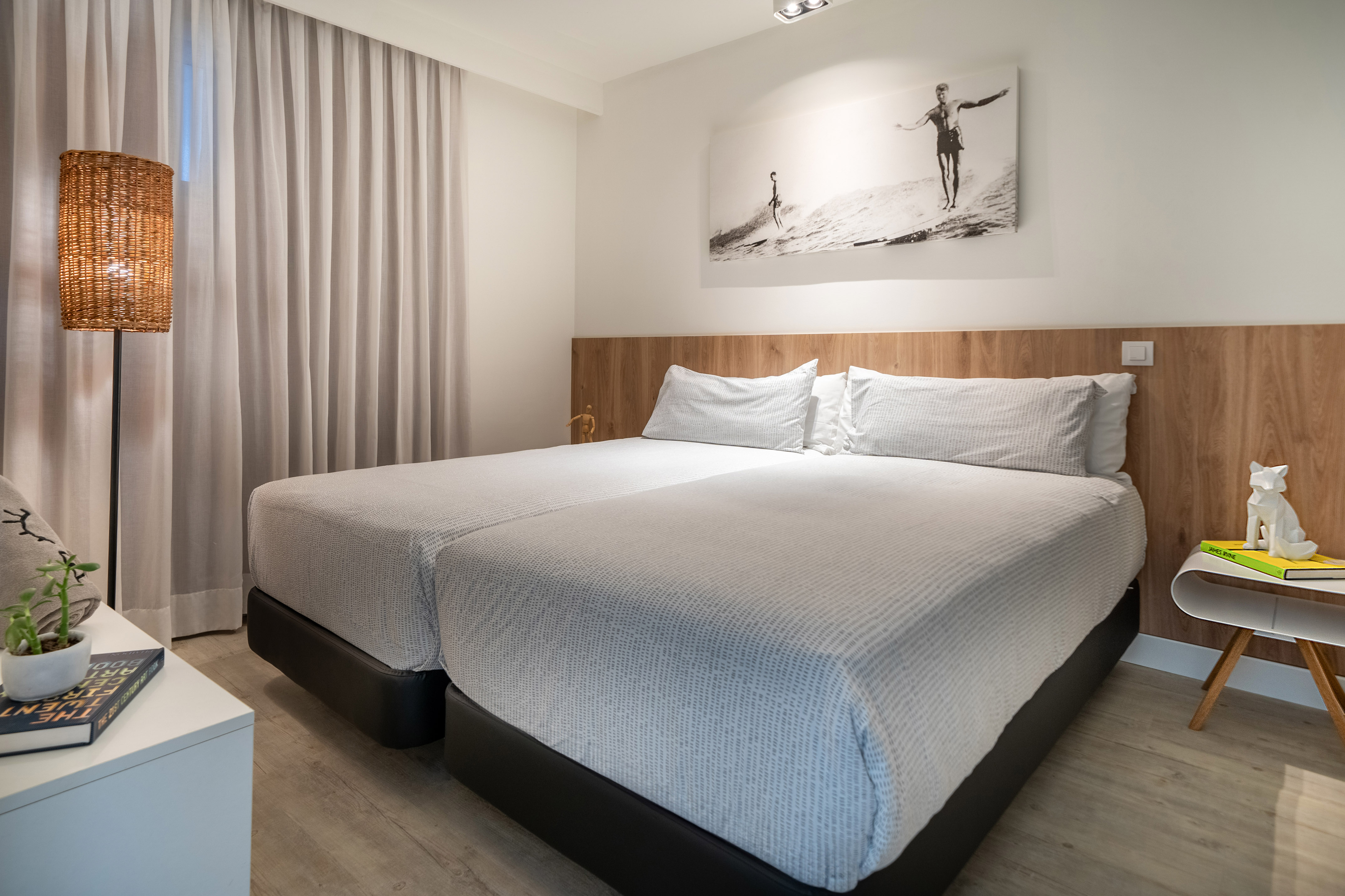 Modern hotel bedroom with white twin beds, wooden headboard, and surfer art.
