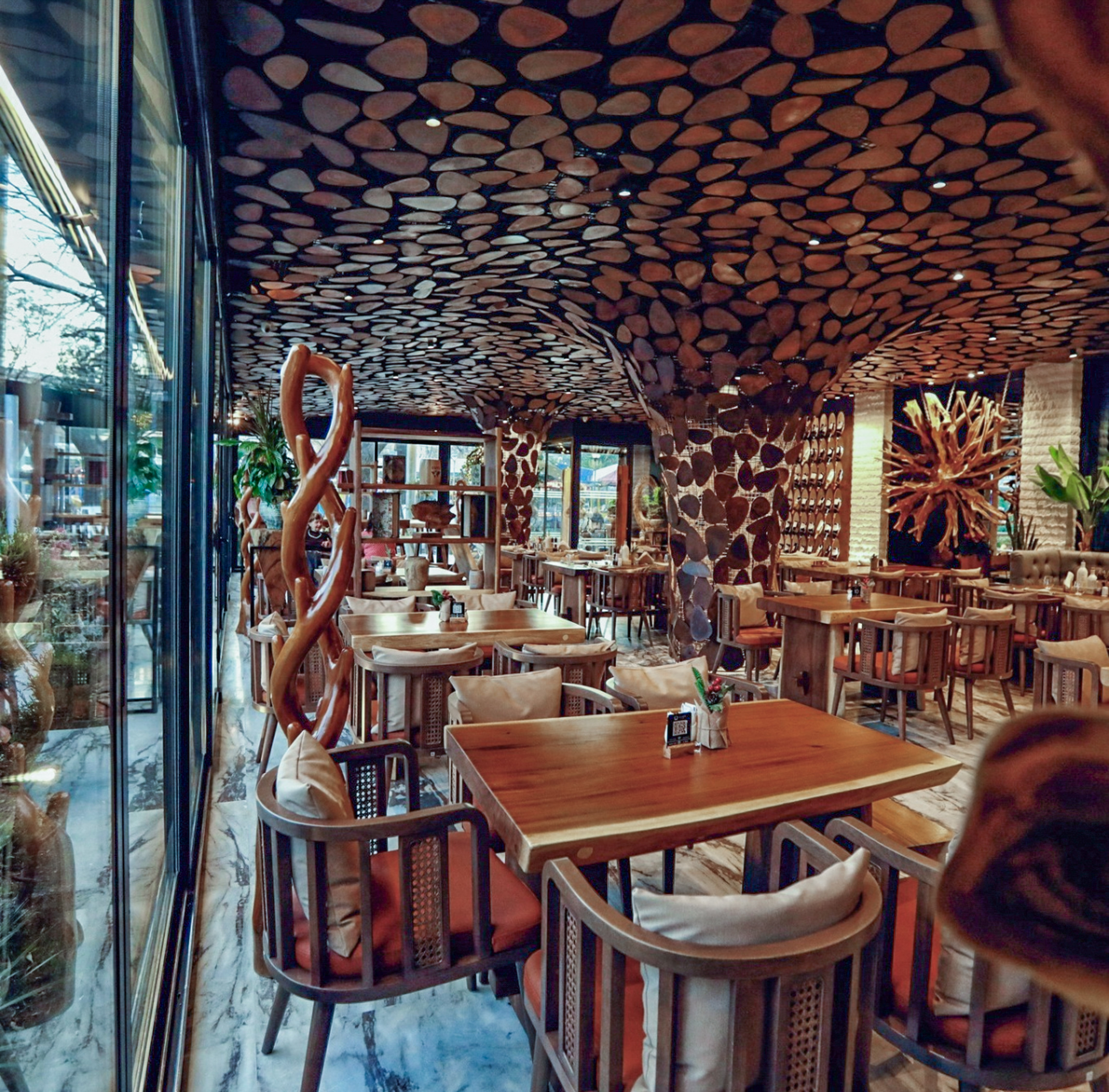 Restaurant interior with unique wood slab ceiling, warm wooden tables and chairs.