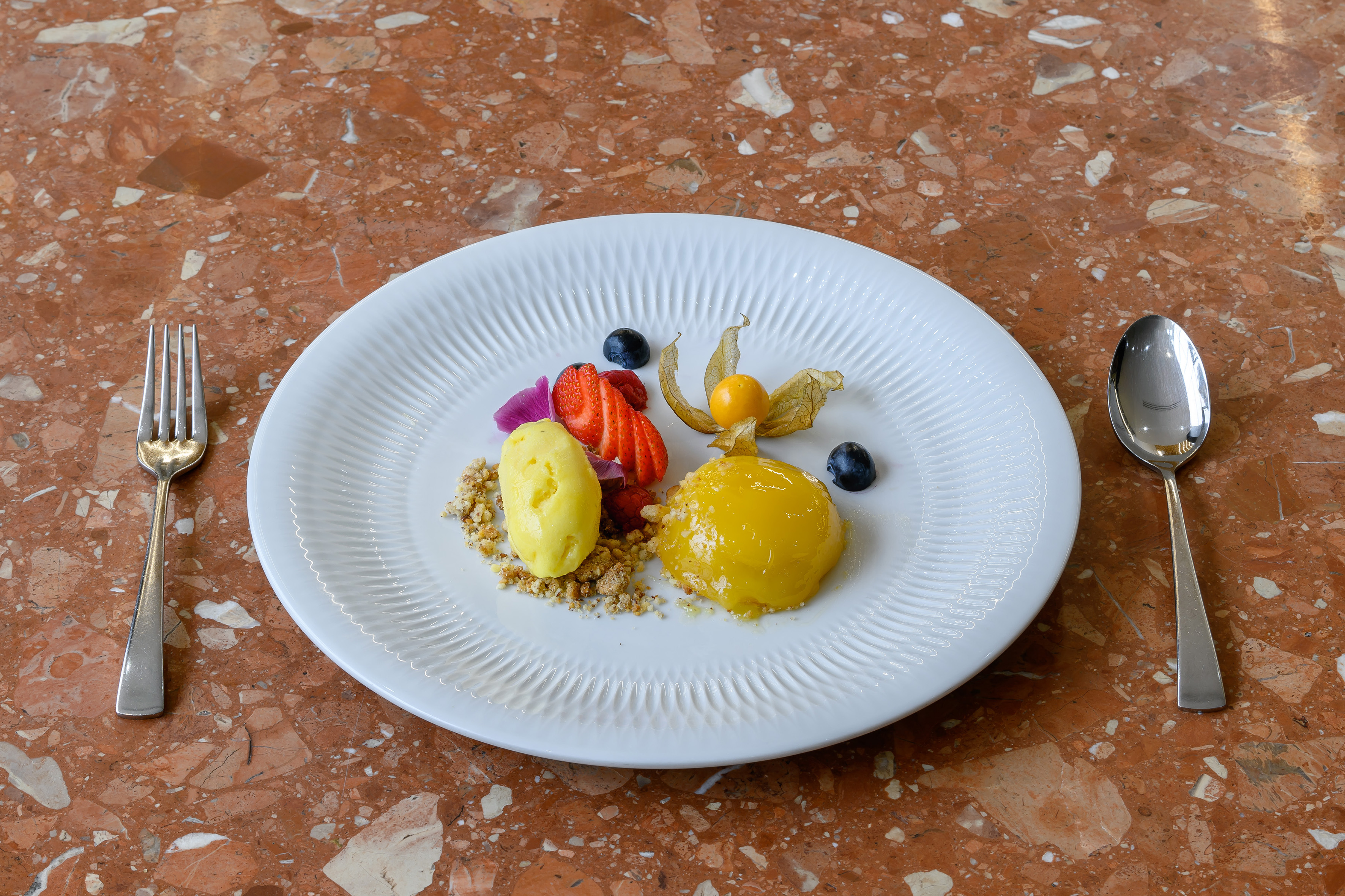 Gourmet plated fruit dessert: yellow sorbet, dome, berries, physalis, crumble.