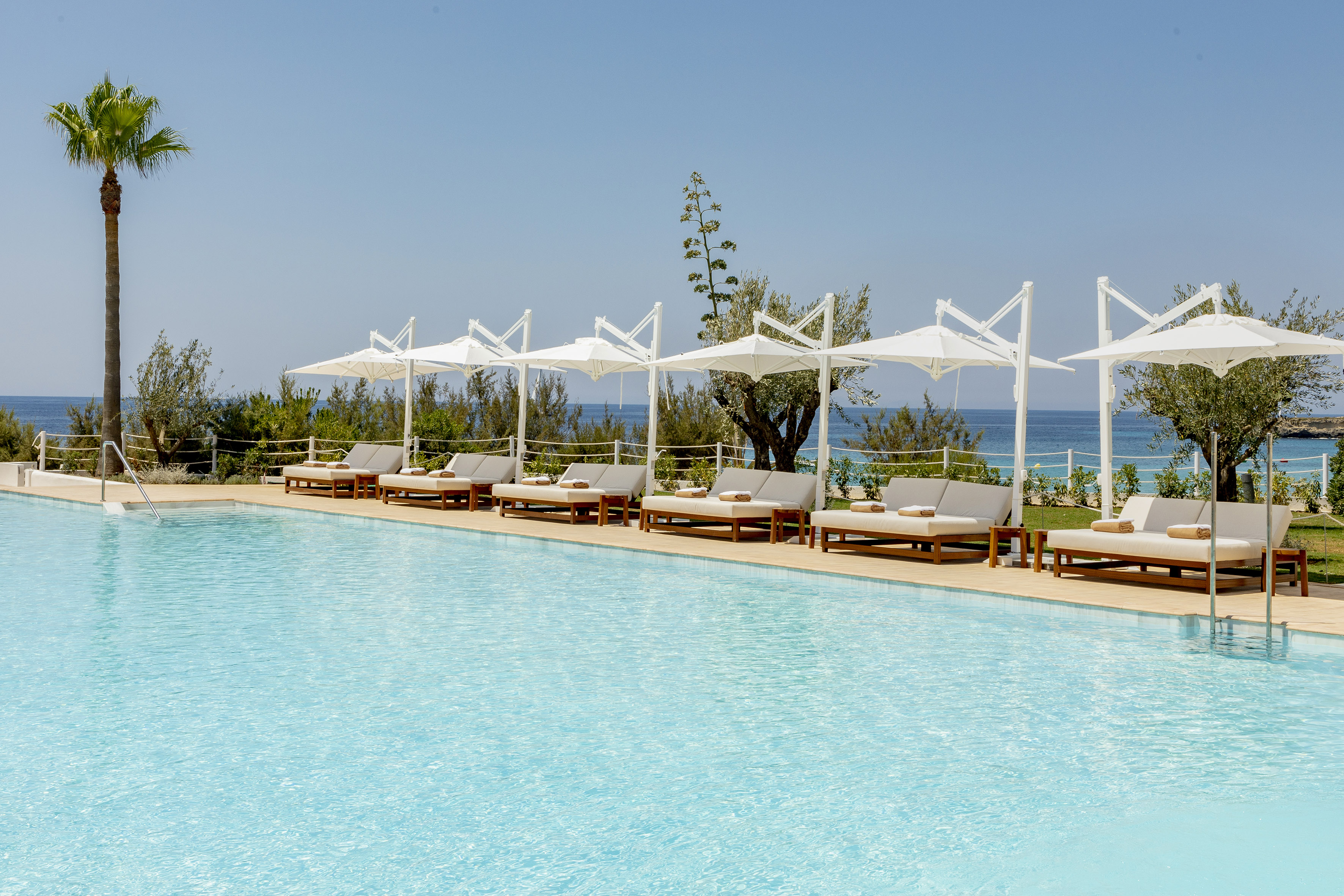 Luxury resort pool deck with sunbeds, white umbrellas, and ocean view.