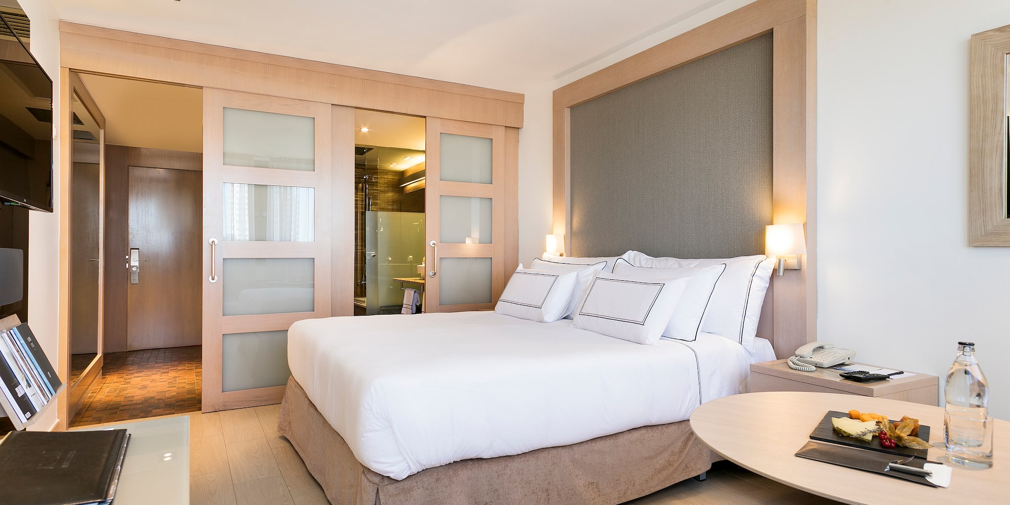 Suite de hotel moderna con cama doble, cabecero de madera y baño integrado.