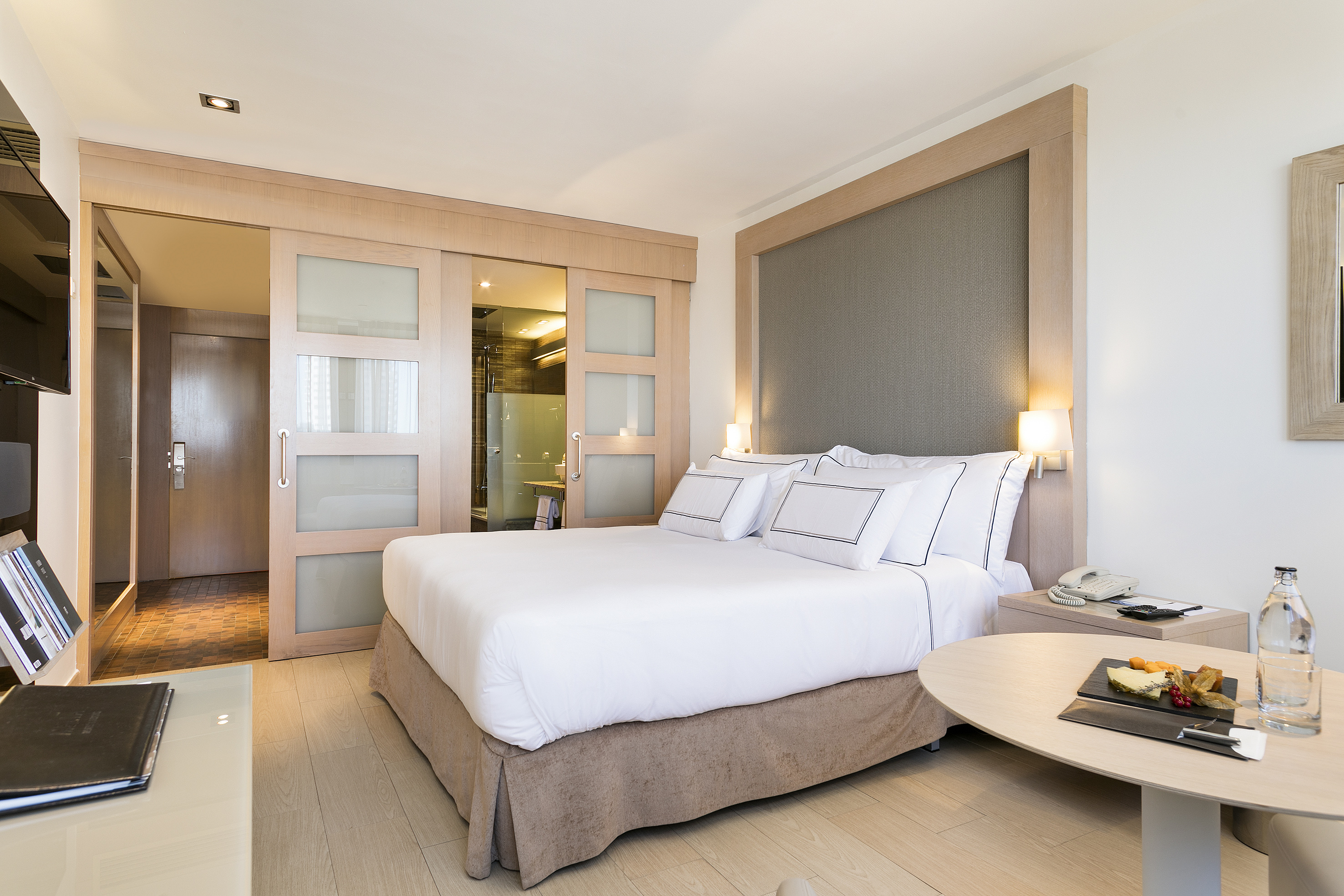 Suite de hotel moderna con cama doble, cabecero de madera y baño integrado.