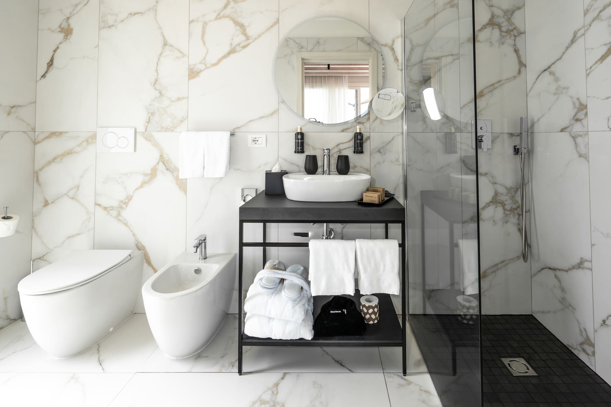 Modern white marble bathroom with black vanity, sink, shower, toilet, and bidet.