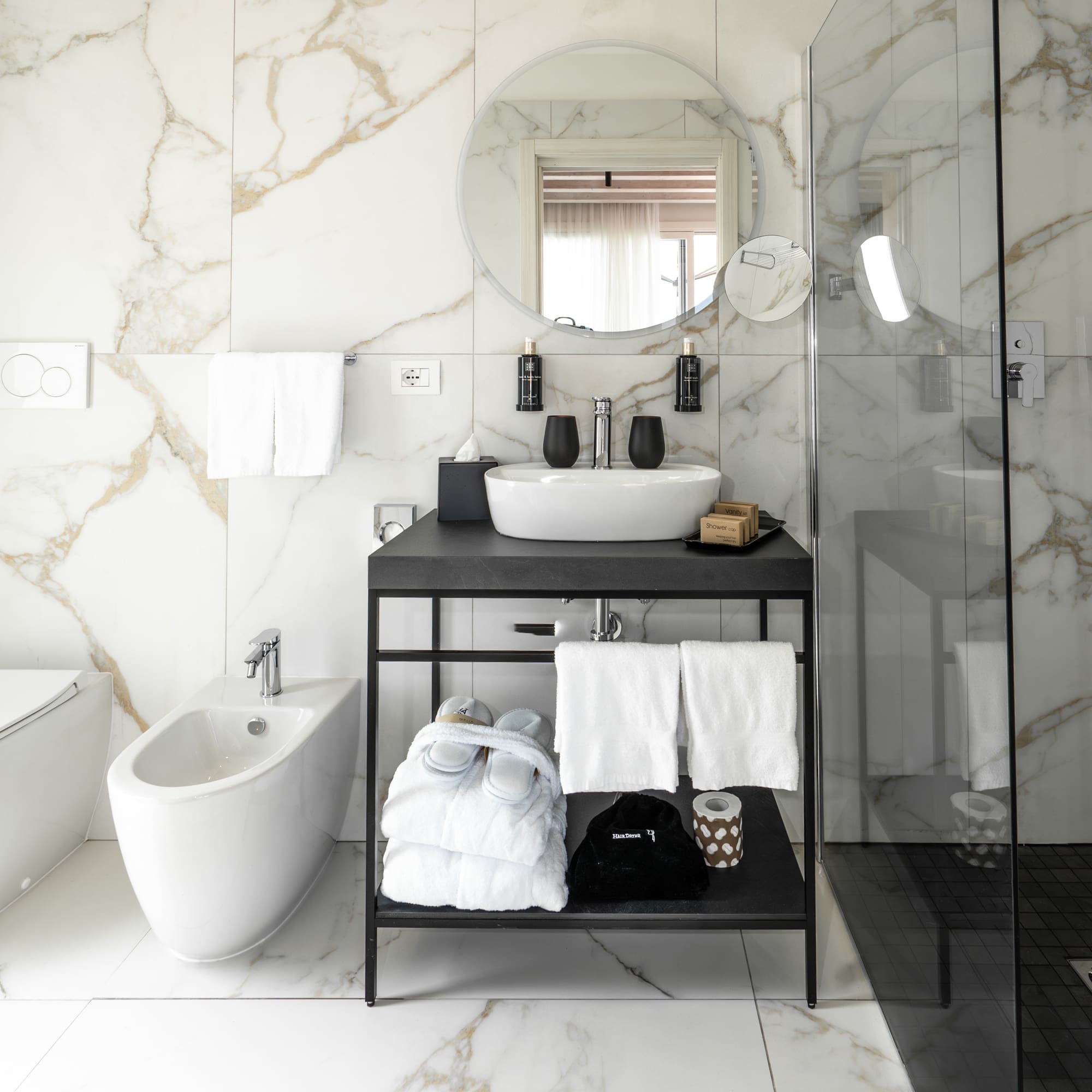 Modern white marble bathroom with black vanity, sink, shower, toilet, and bidet.