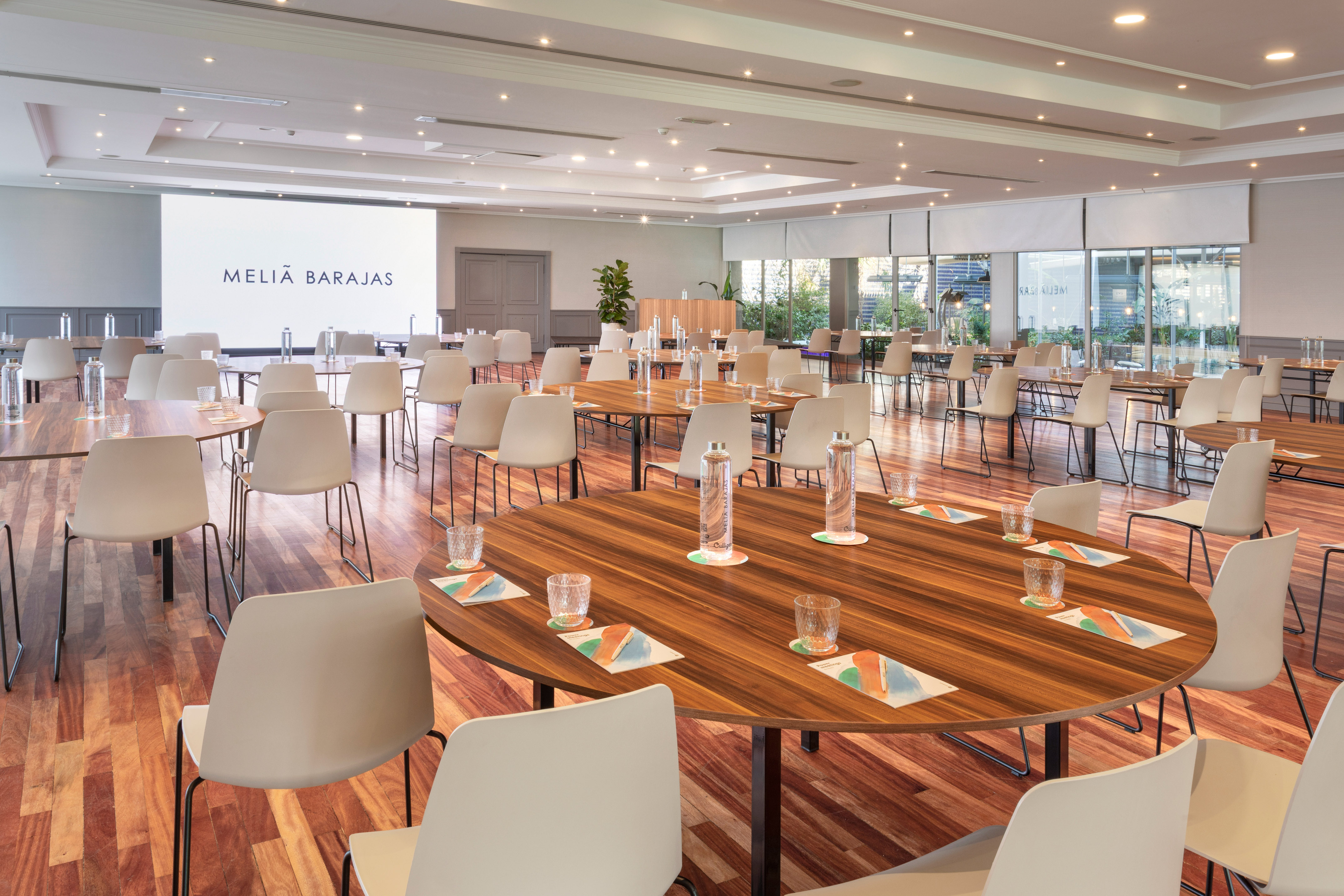 Meliá Barajas hotel meeting room with round tables, chairs, and large screen.