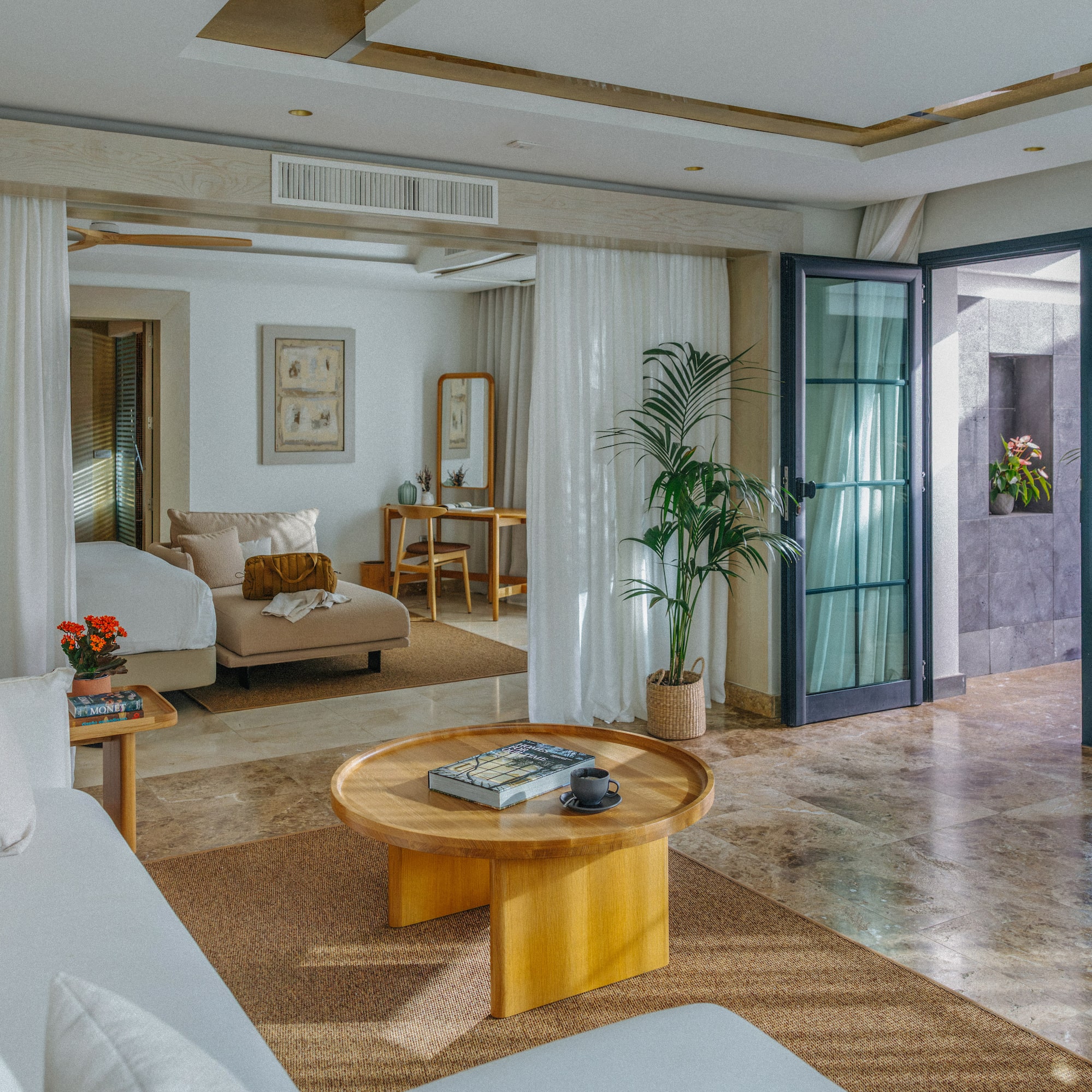 Modern luxury suite: open living area, white sofa, wood table, plant decor.