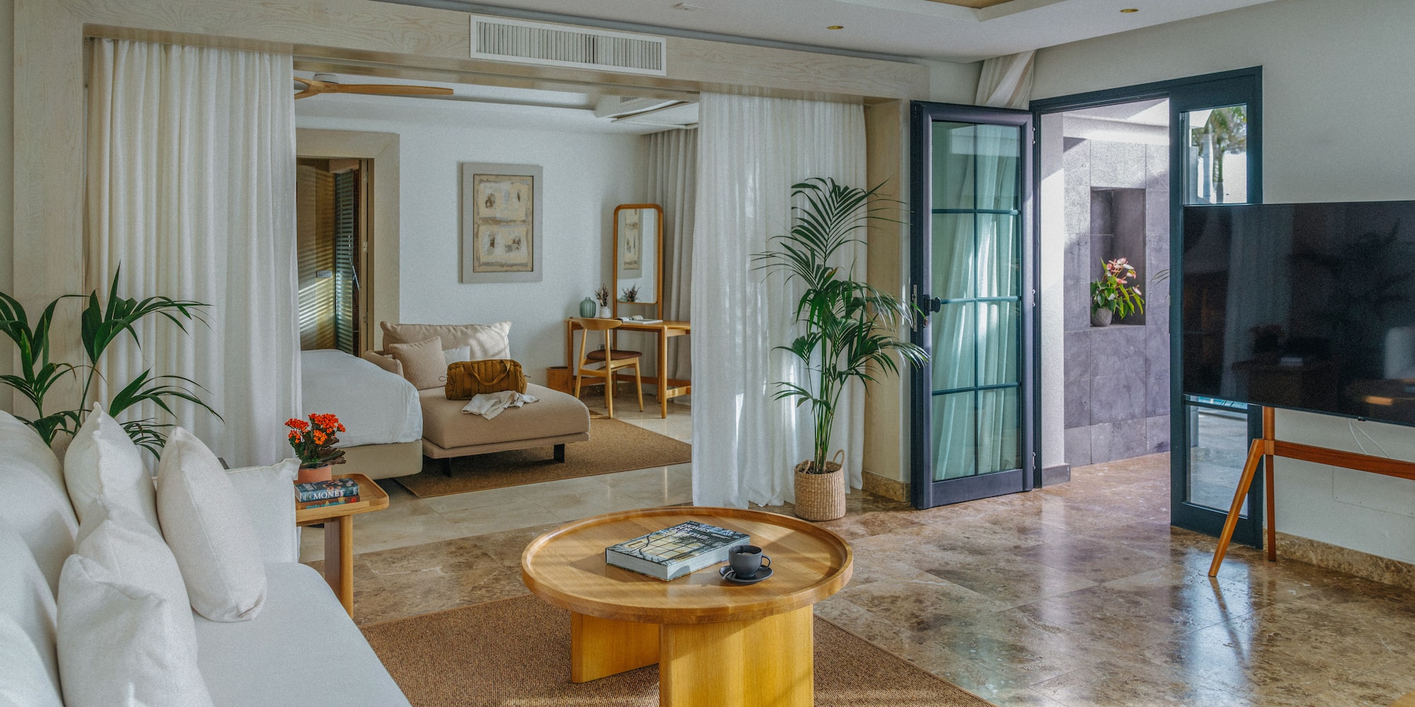 Modern luxury suite: open living area, white sofa, wood table, plant decor.