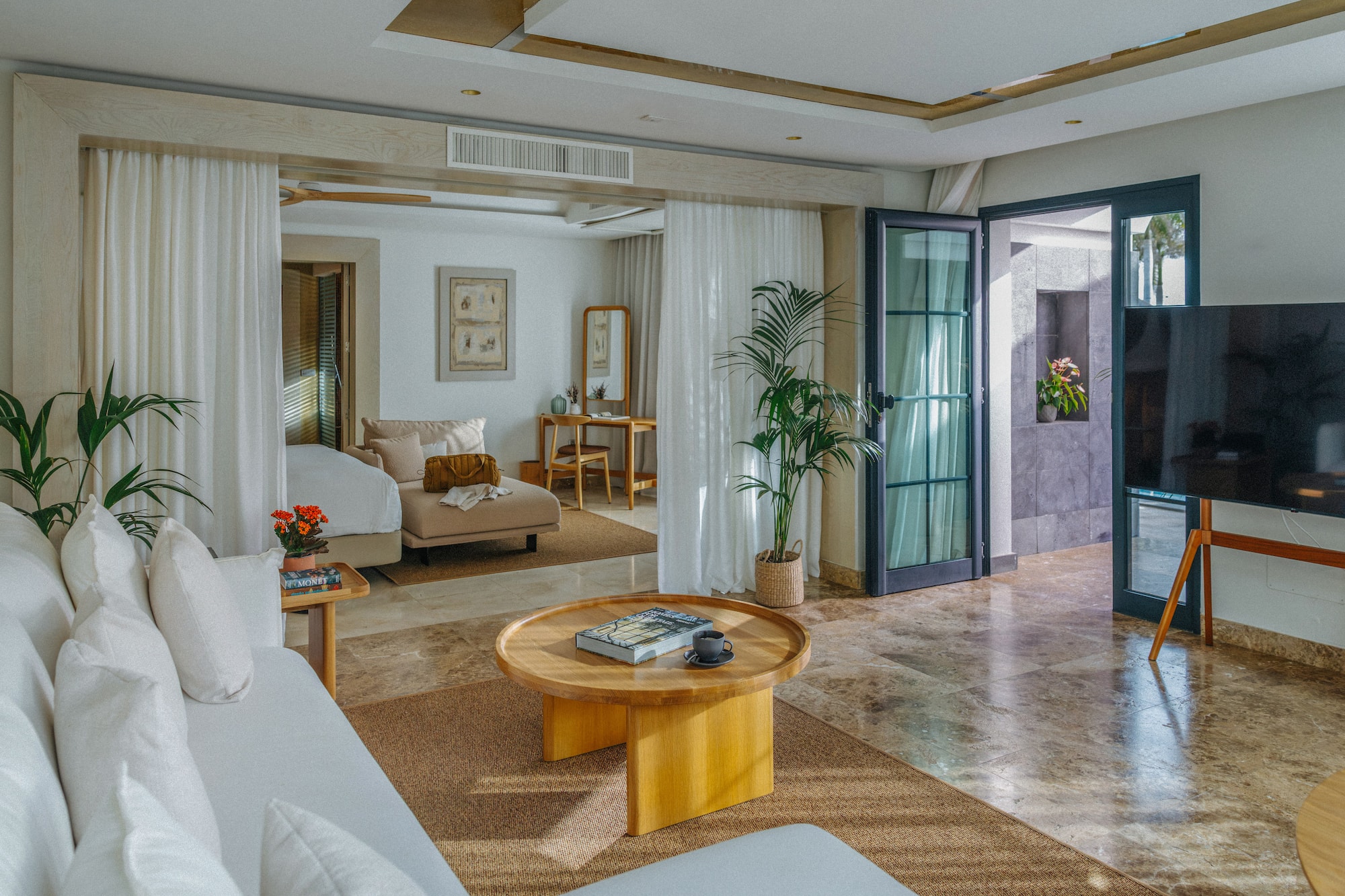 Modern luxury suite: open living area, white sofa, wood table, plant decor.