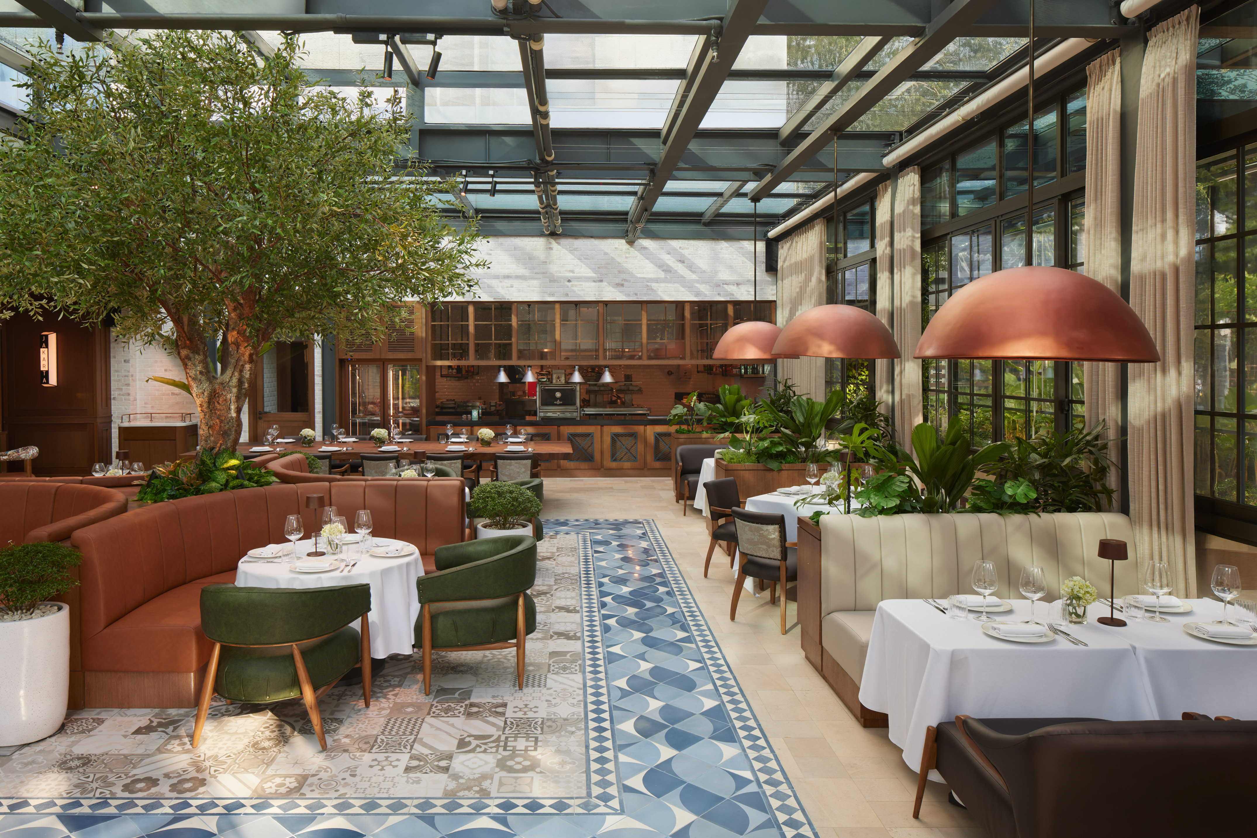 Upscale restaurant with indoor tree, glass roof, modern seating, and open kitchen.