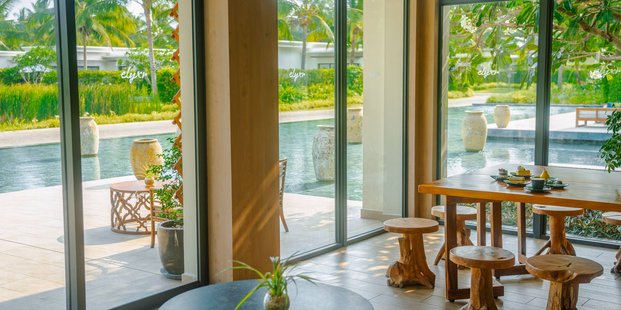 Resort dining with tropical pool view, palm trees, and unique wooden stools.
