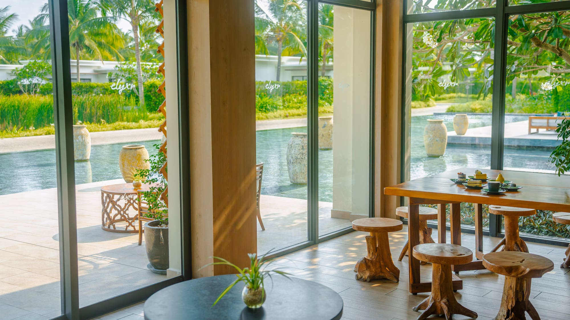Resort dining with tropical pool view, palm trees, and unique wooden stools.