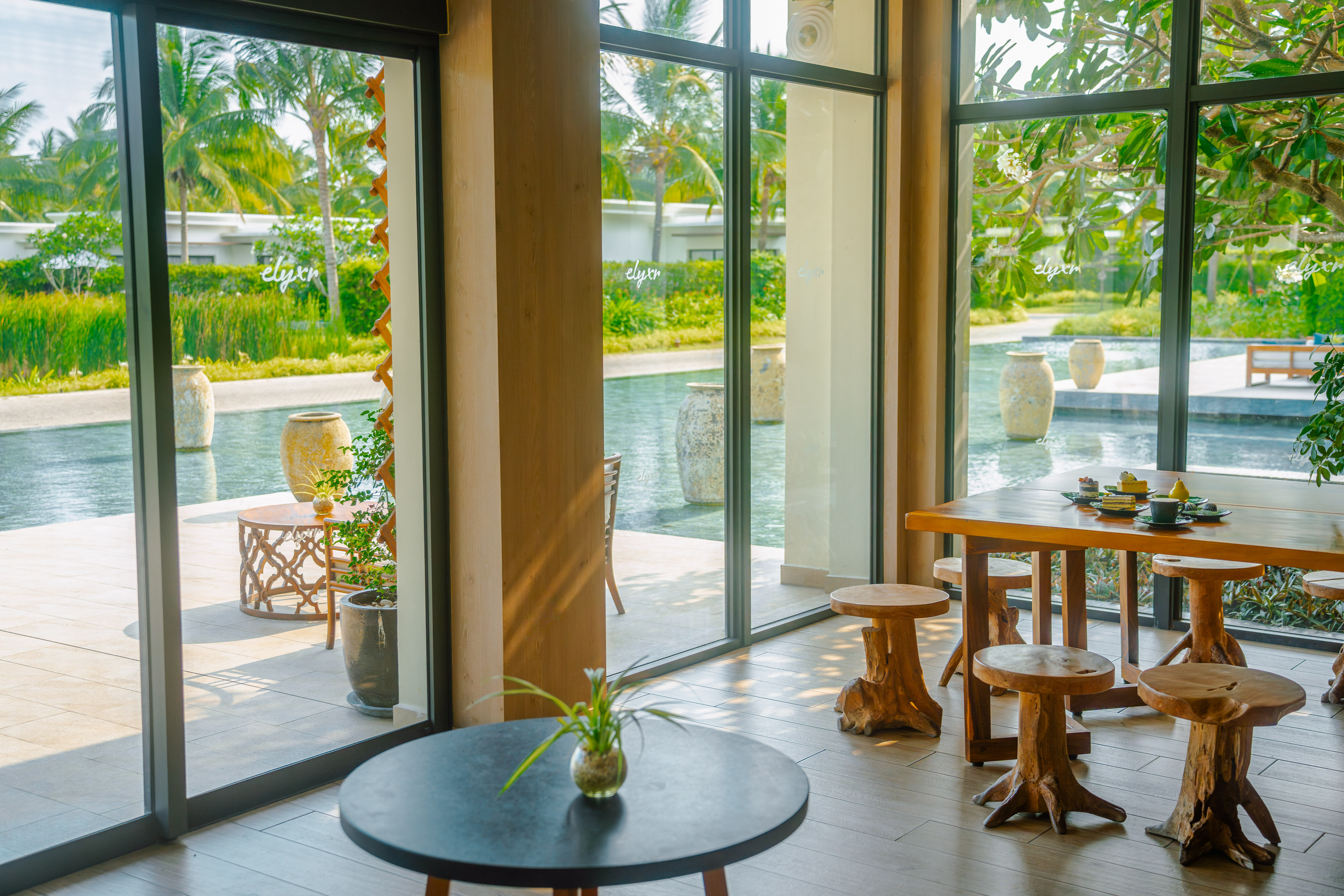 Resort dining with tropical pool view, palm trees, and unique wooden stools.