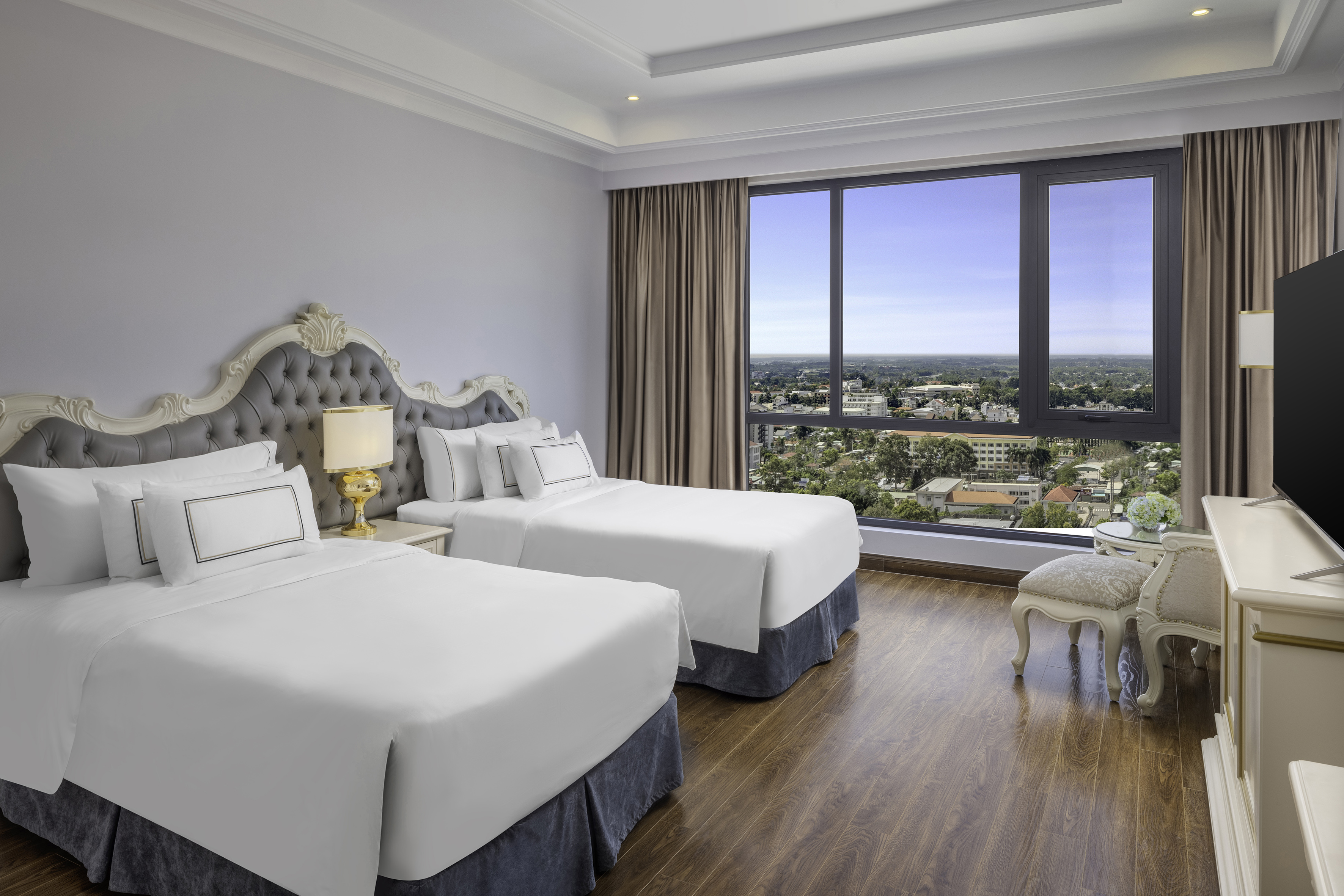 Luxury hotel room with two twin beds, ornate headboards, and a city view window.