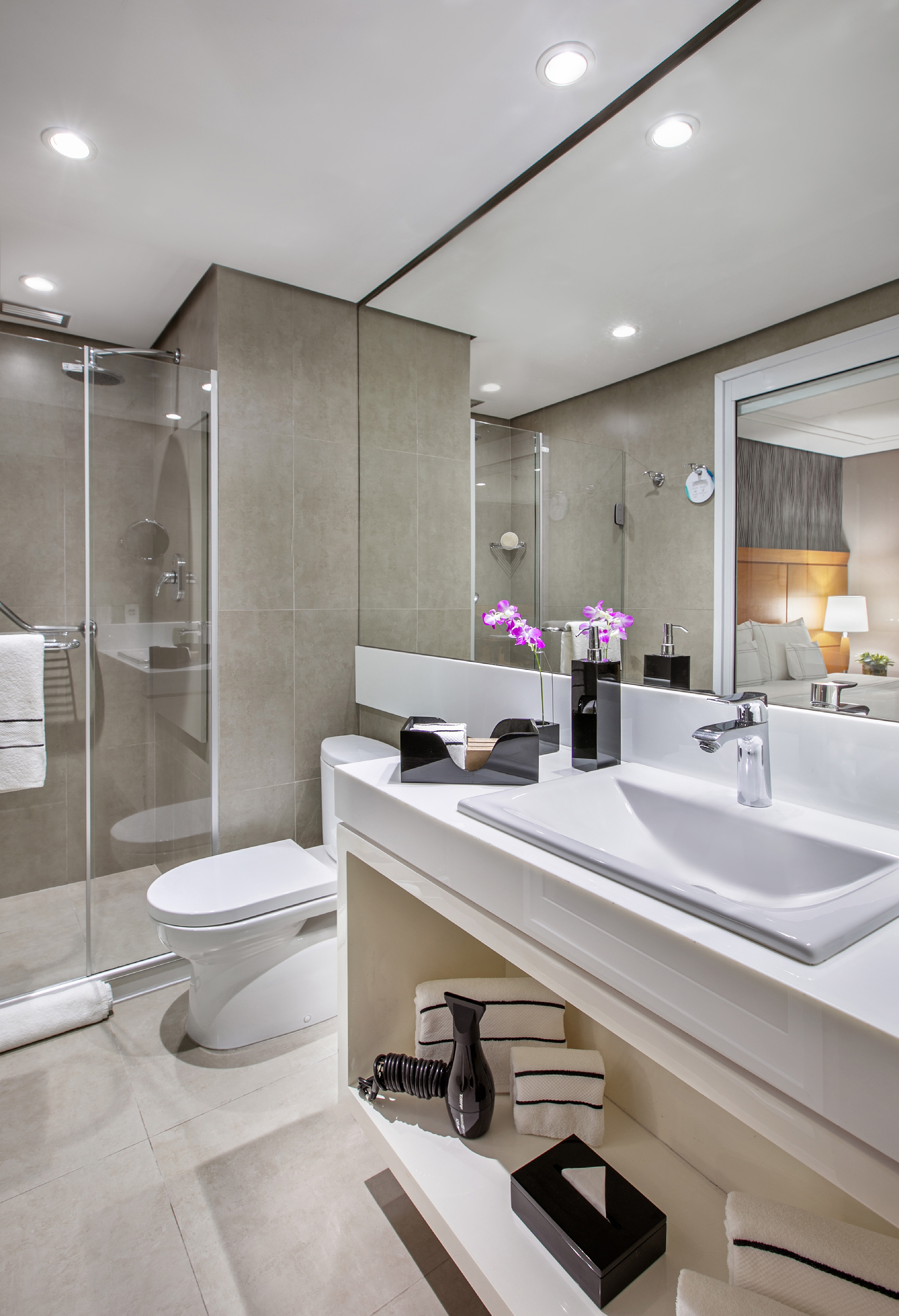 Modern hotel bathroom with white vanity, sink, toilet, glass shower, and purple orchids.