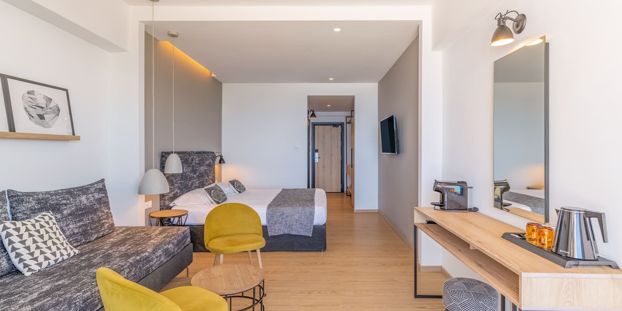 Contemporary hotel suite with sofa, bed, and desk.