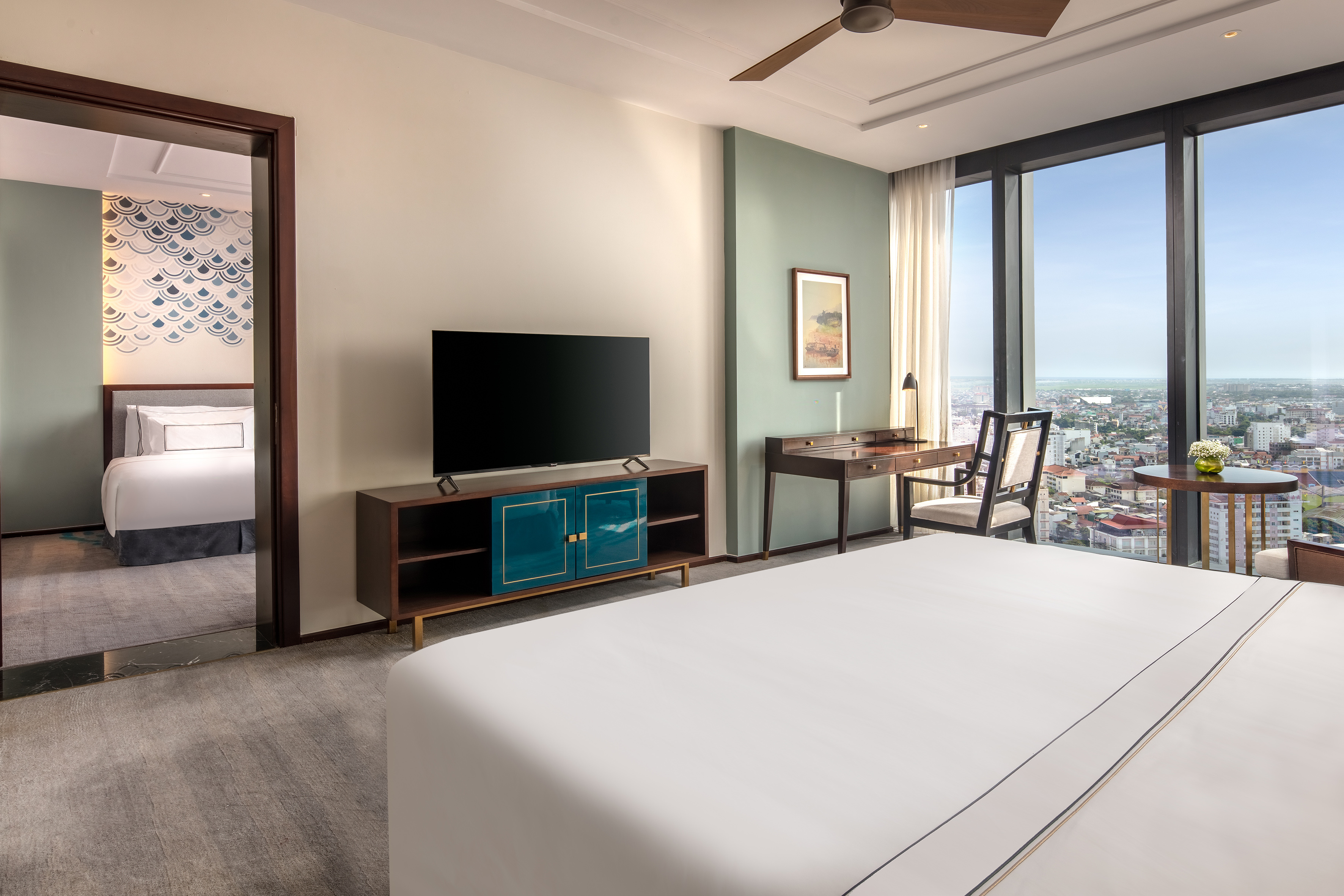 Modern hotel suite with panoramic city view, king bed, desk, and adjoining room.