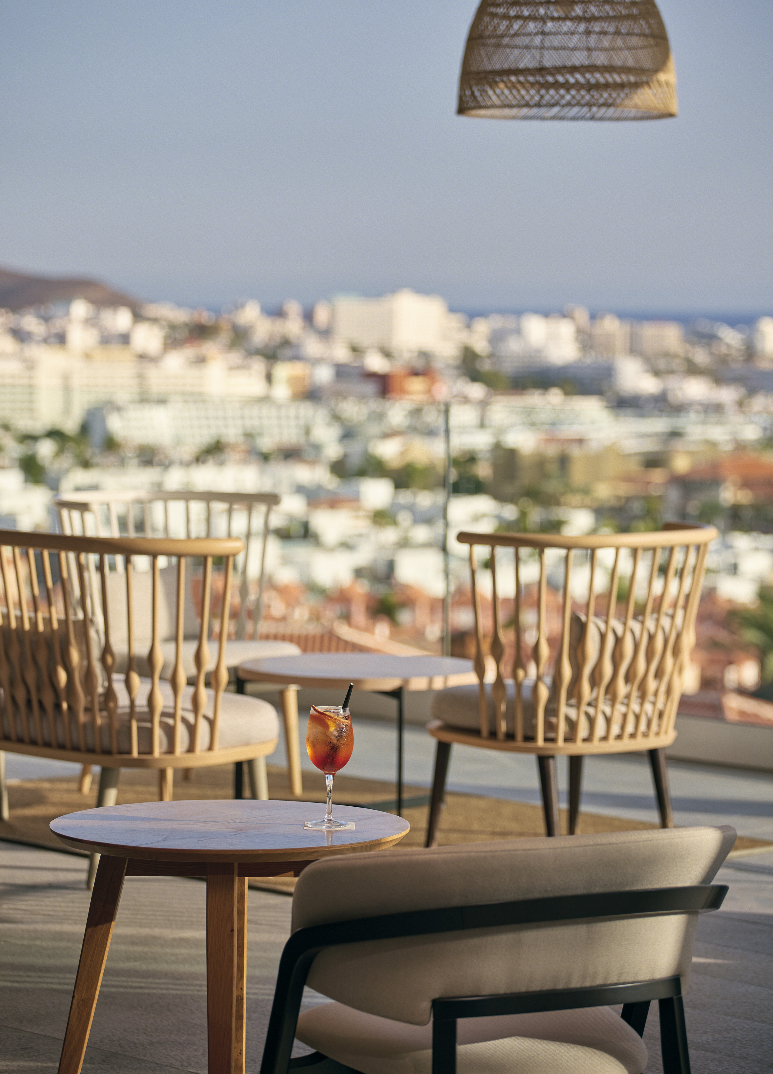 Hotel terrace with cocktail, modern furniture, cityscape, and sea view.