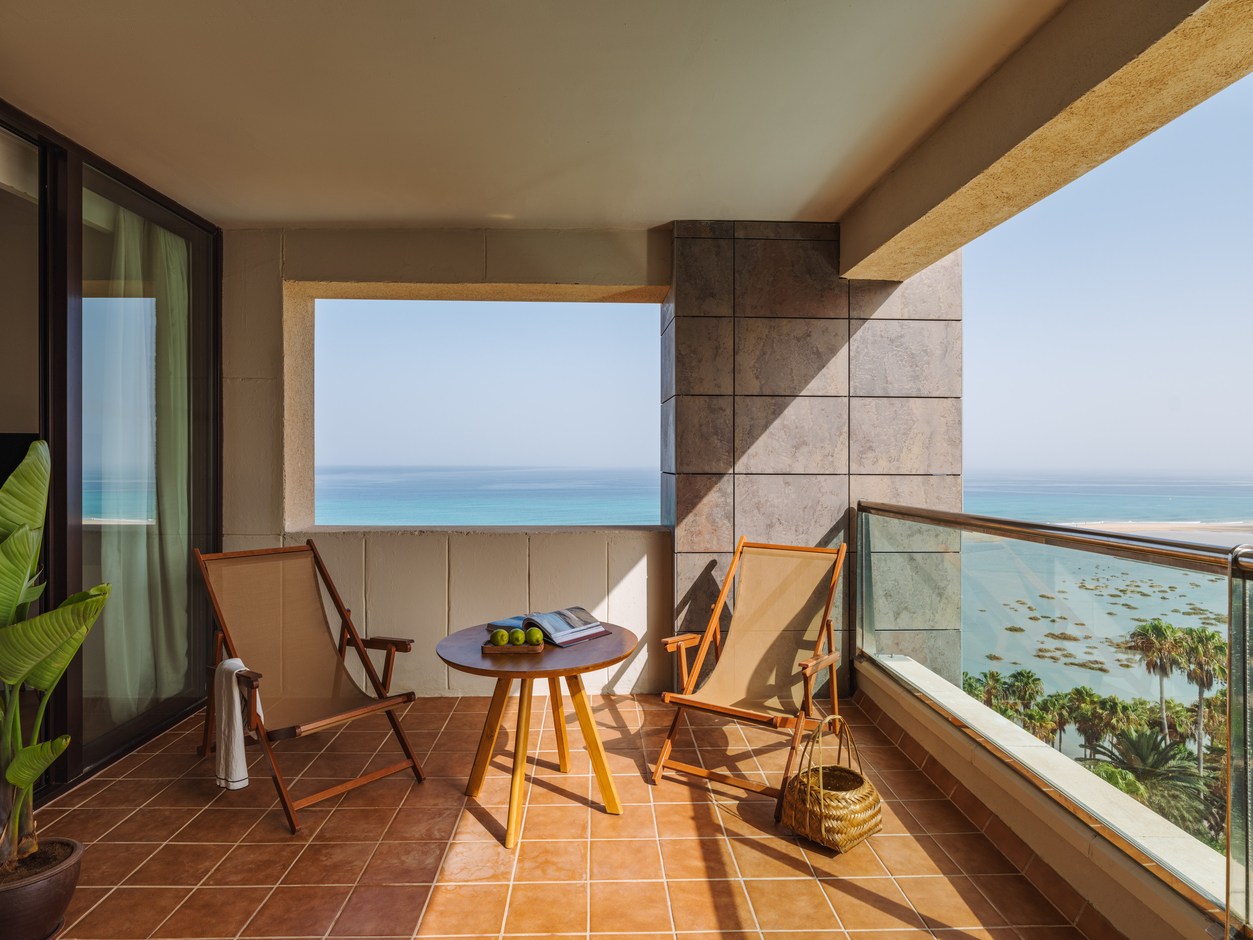 Ocean view resort balcony with two chairs, table, and palm trees.