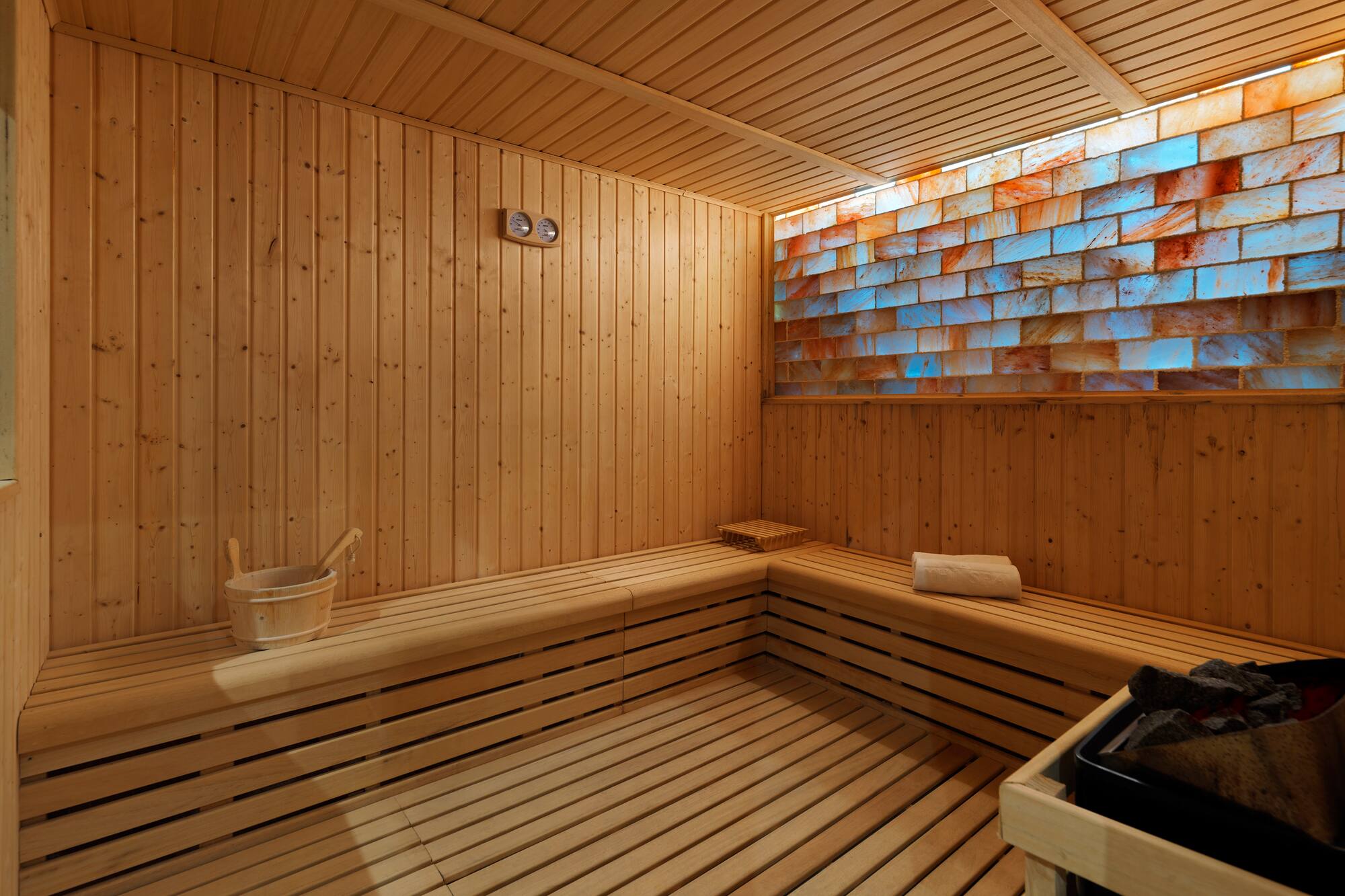 Modern wooden sauna with illuminated Himalayan salt brick wall and benches.