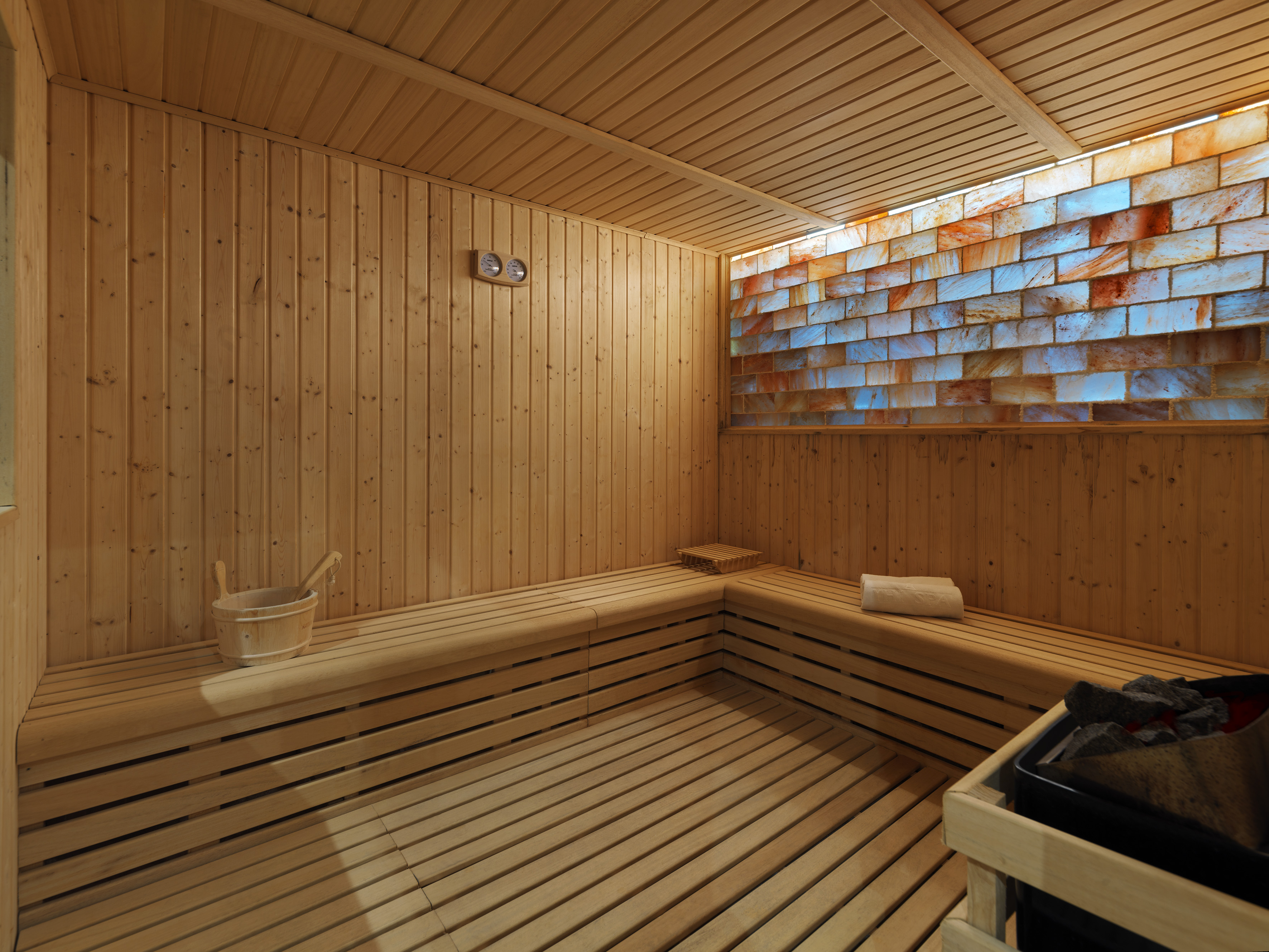 Modern wooden sauna with illuminated Himalayan salt brick wall and benches.