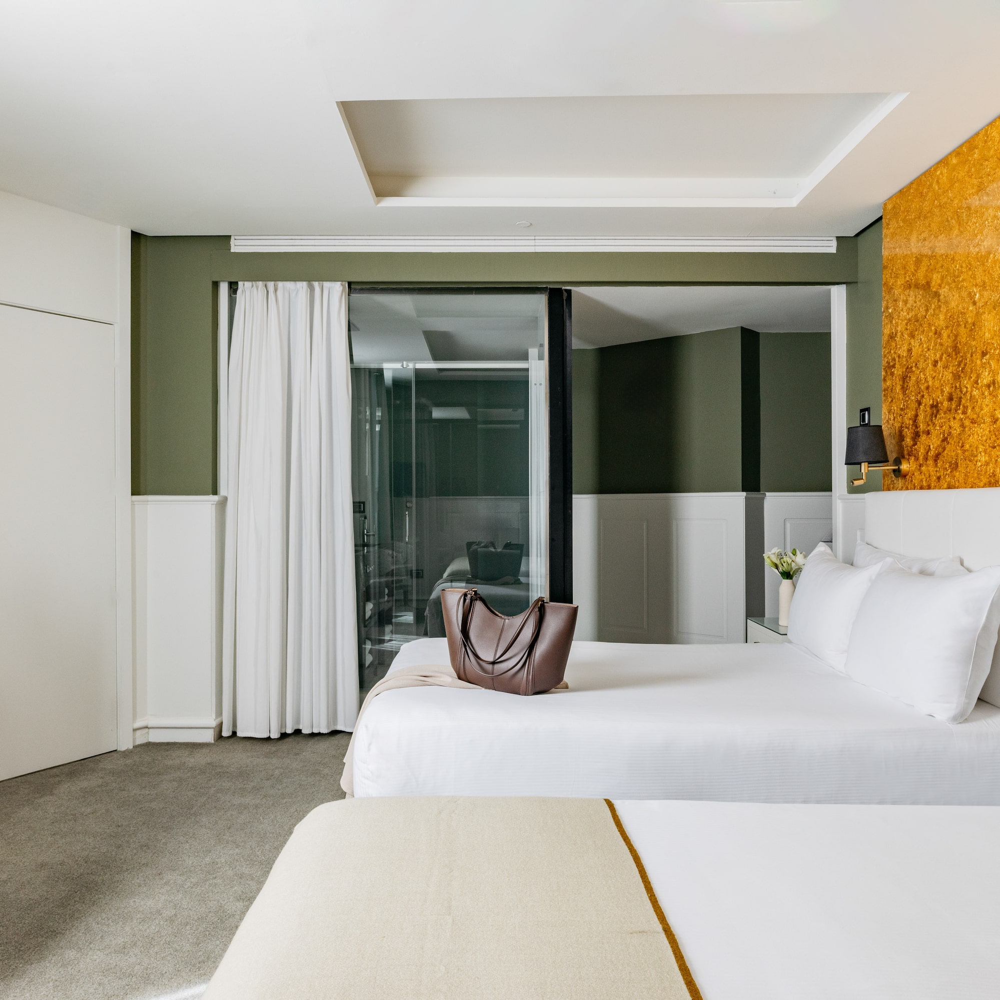 Habitación de hotel moderna con dos camas, paredes verdes y acento dorado.