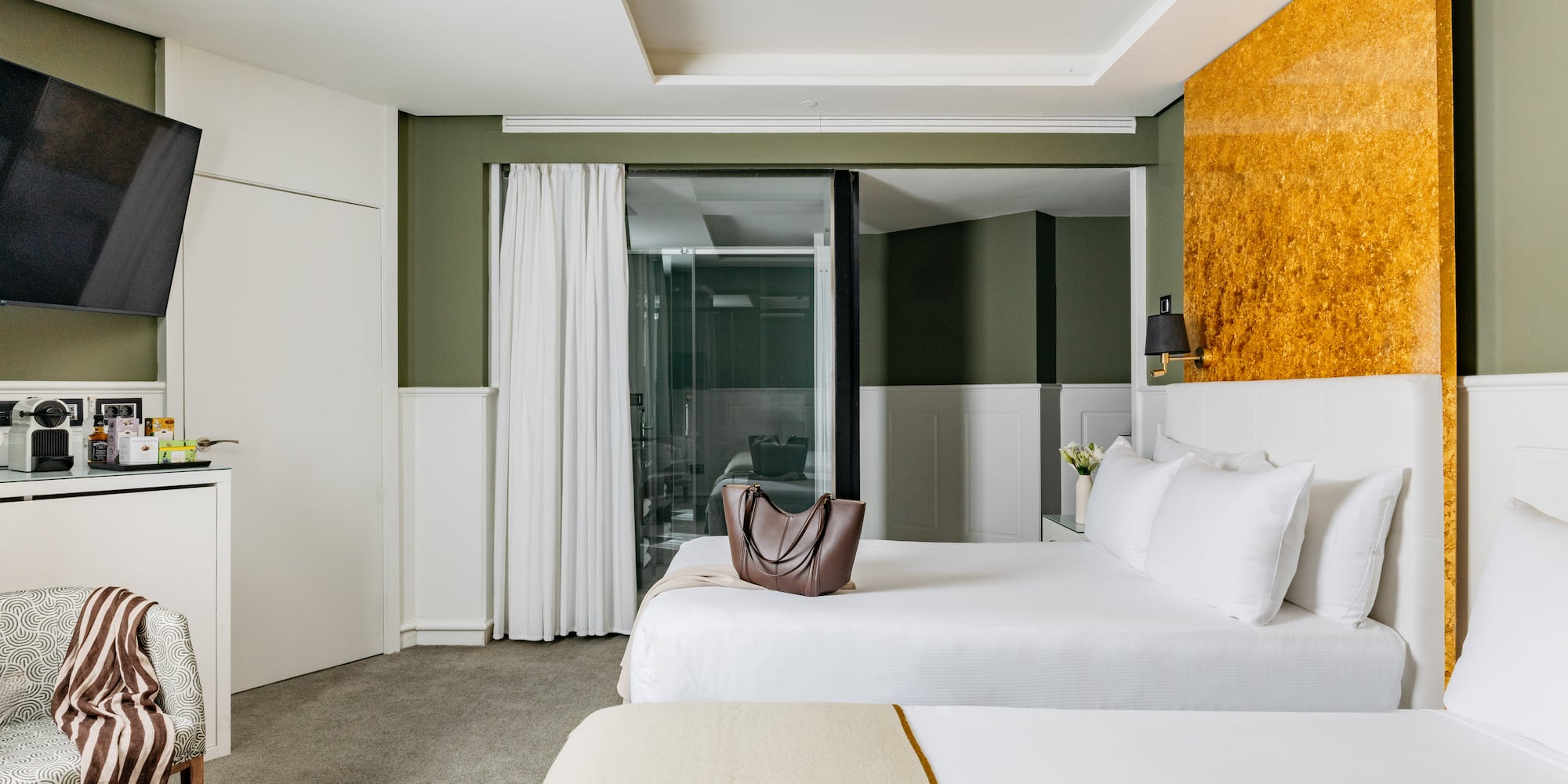 Habitación de hotel moderna con dos camas, paredes verdes y acento dorado.