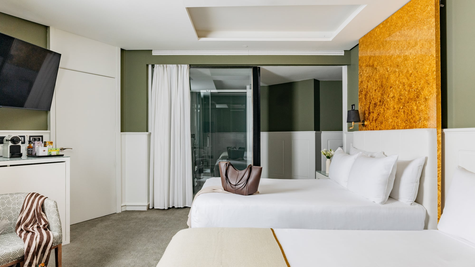 Habitación de hotel moderna con dos camas, paredes verdes y acento dorado.