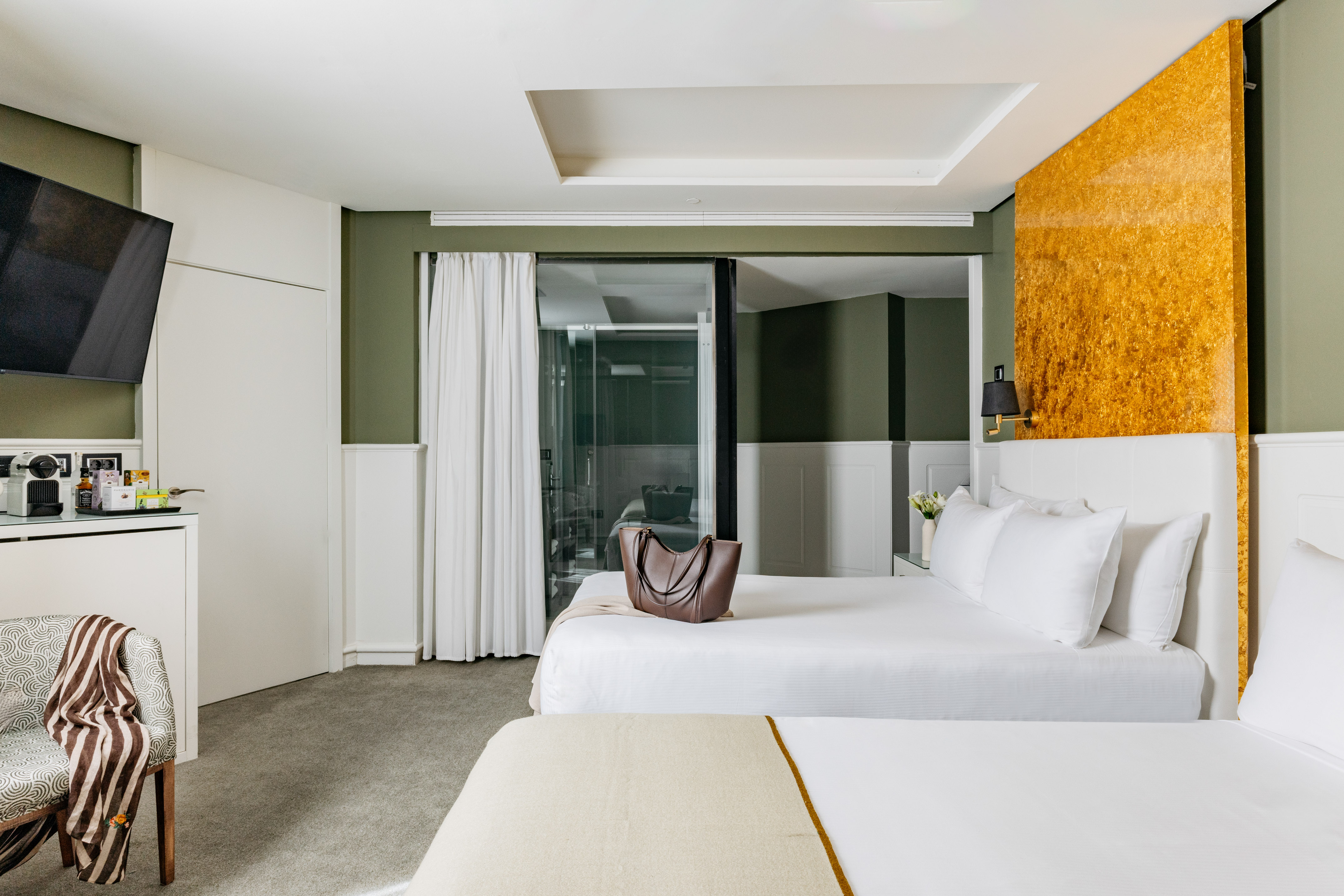 Habitación de hotel moderna con dos camas, paredes verdes y acento dorado.