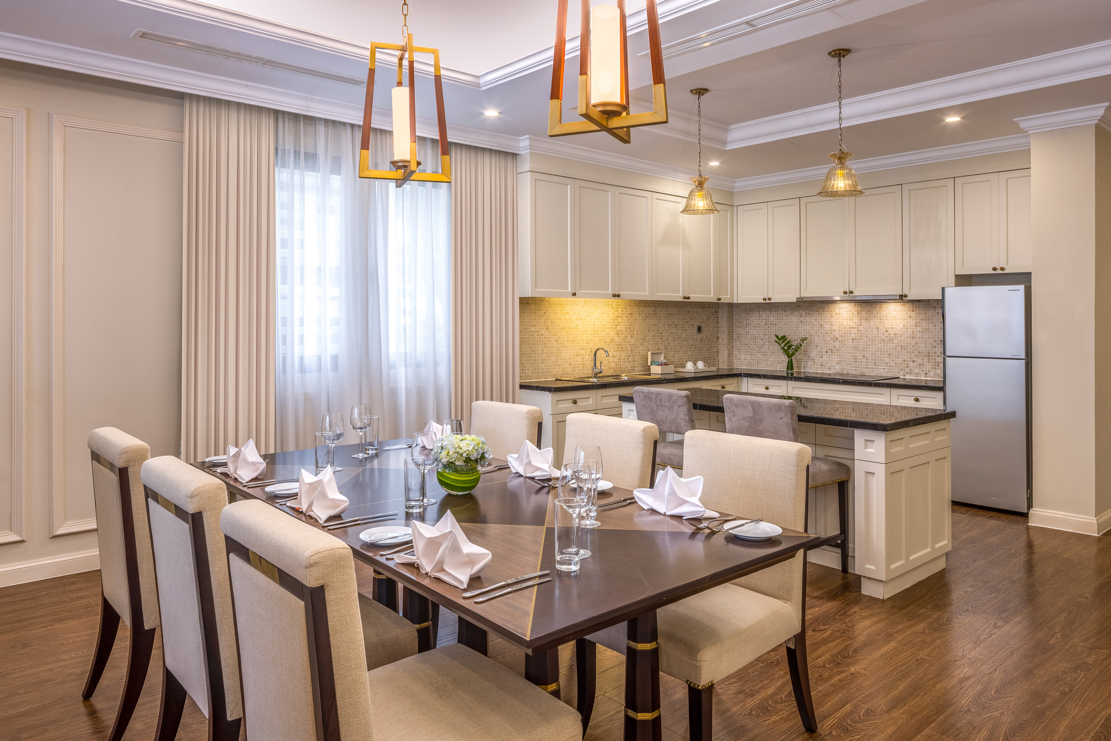 Modern dining room and open kitchen with set table and elegant pendant lights.