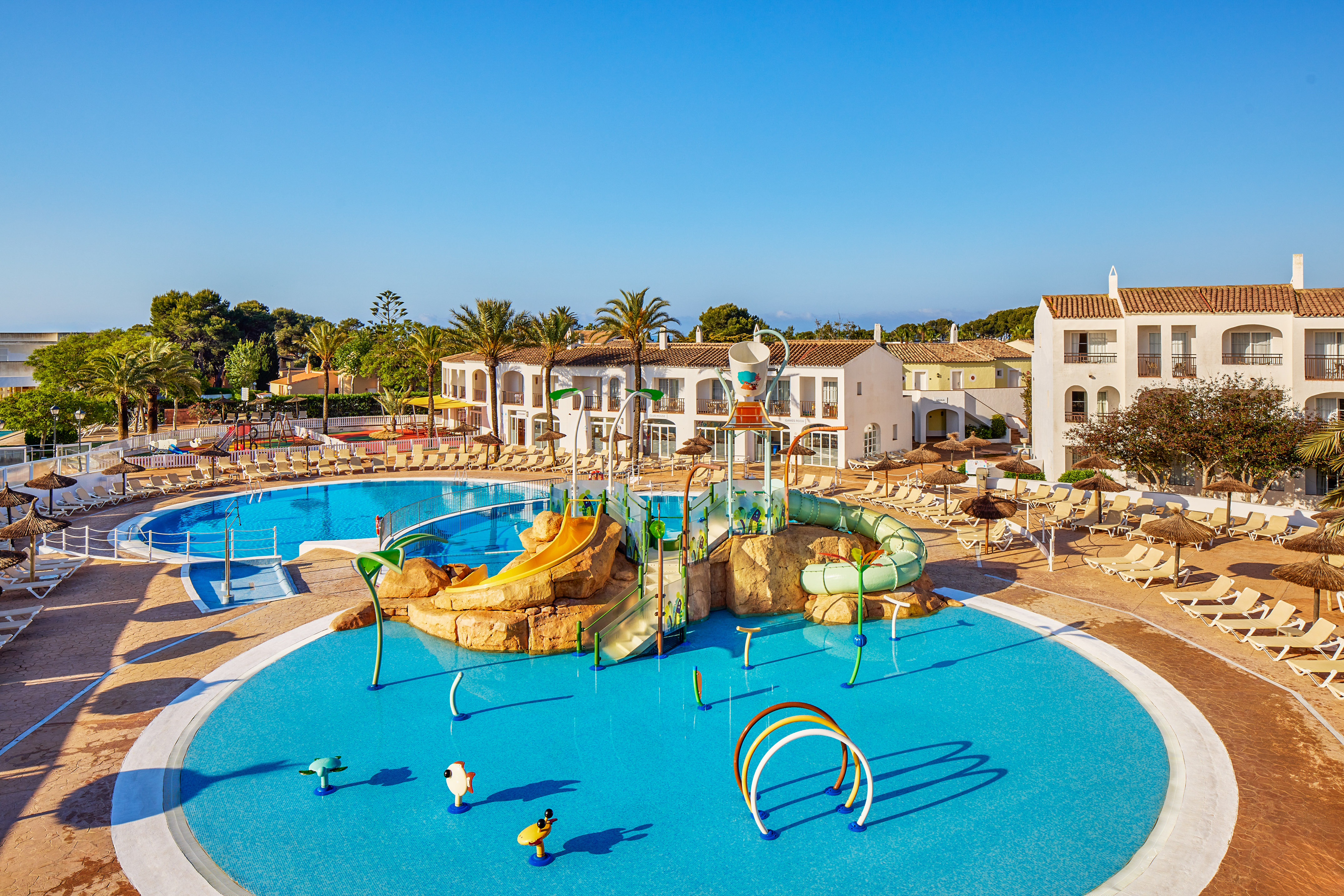 Sunny family resort with water park, multiple pools, hotel buildings, and palm trees.