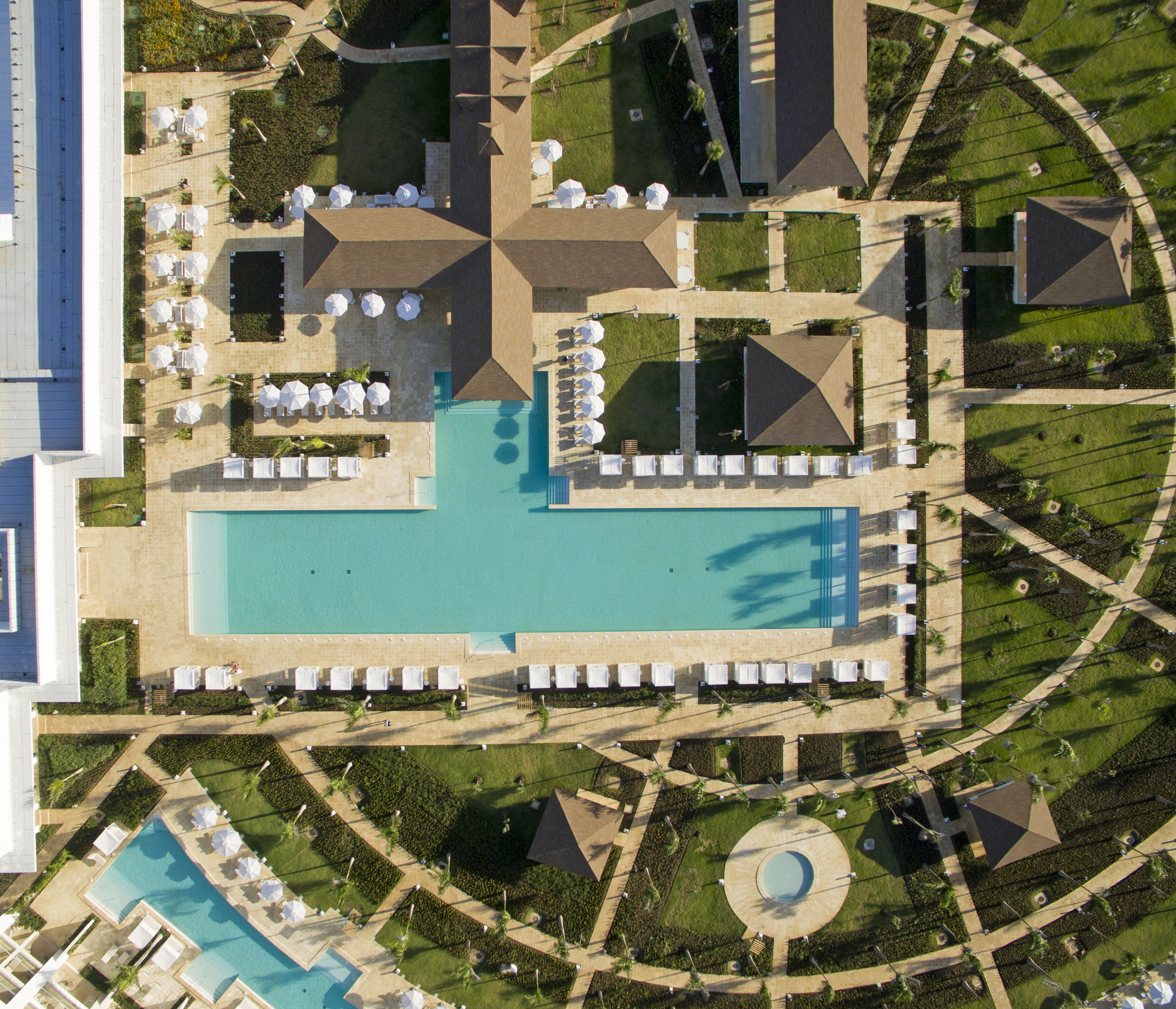 Aerial view of a luxury resort with large swimming pools, lush gardens, and buildings.