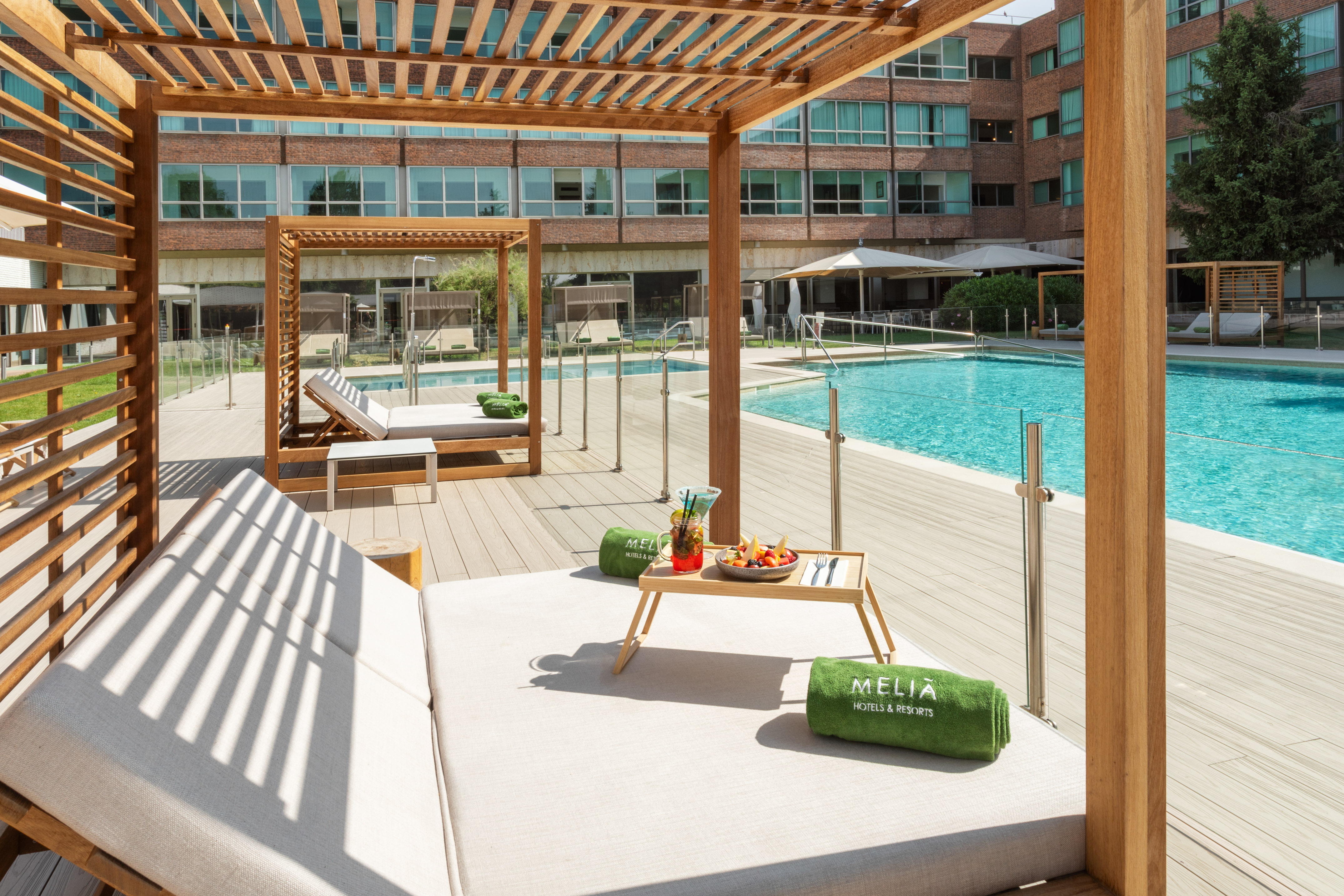 Meliá hotel outdoor pool with wooden pergolas, daybeds, and cocktails.