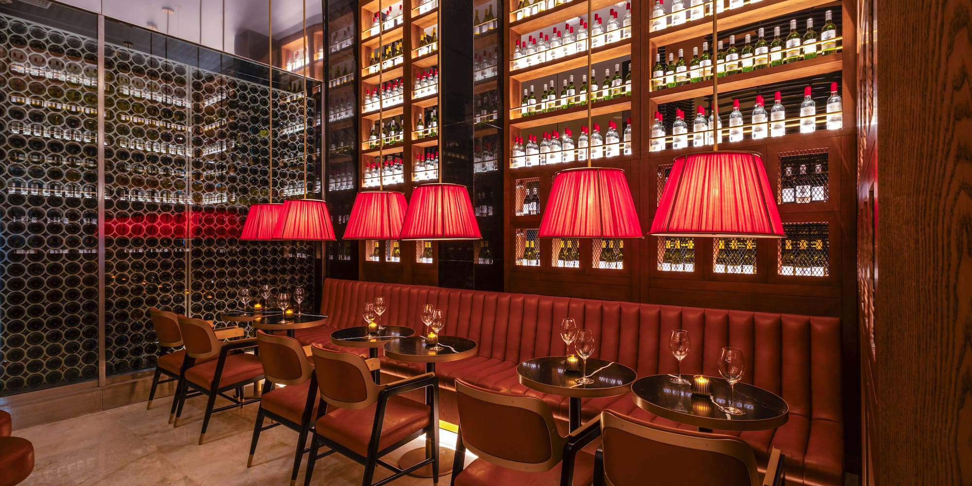 Upscale bar interior with red seating, pendant lights, and wall-to-wall wine displays.