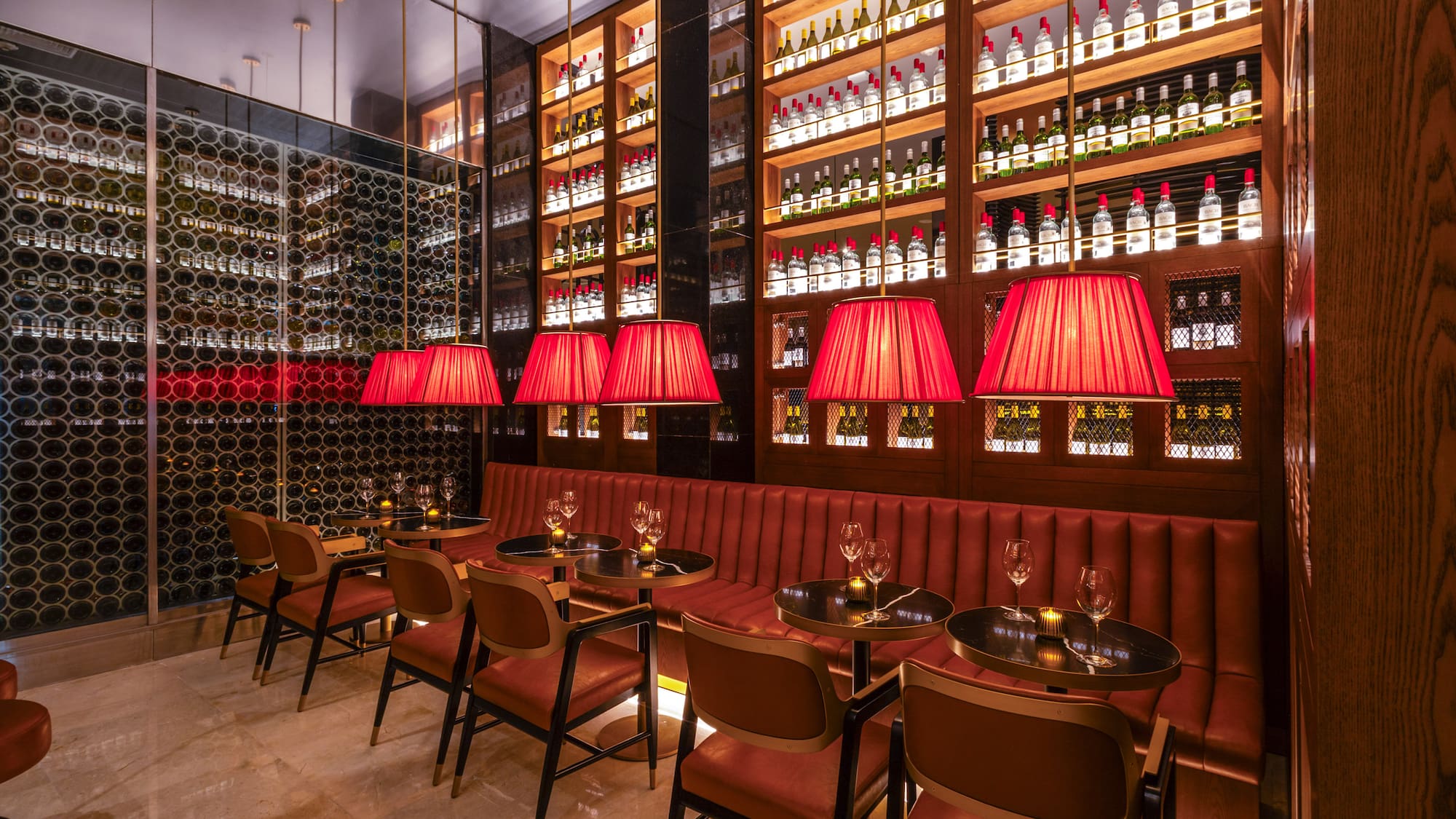 Upscale bar interior with red seating, pendant lights, and wall-to-wall wine displays.