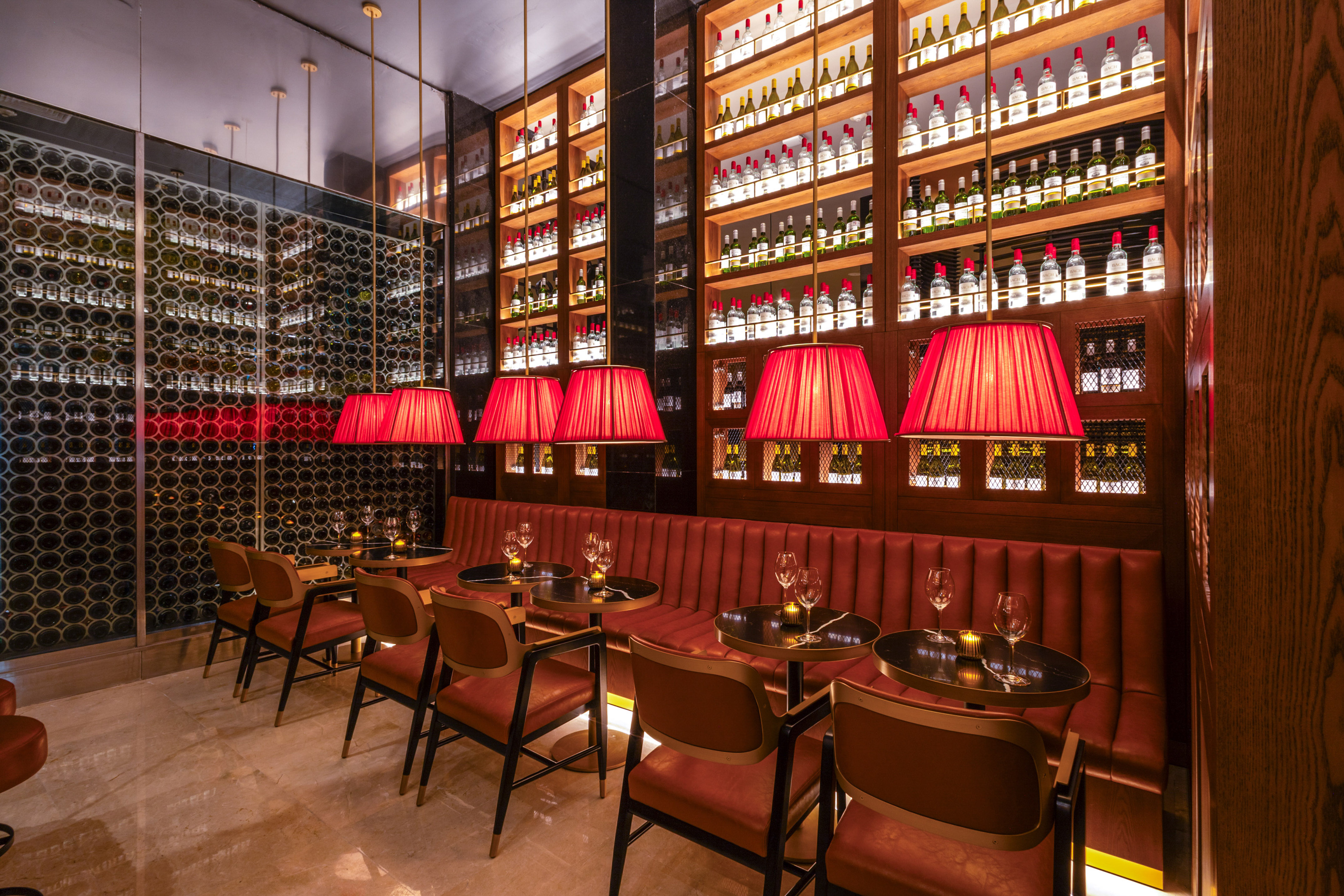 Upscale bar interior with red seating, pendant lights, and wall-to-wall wine displays.