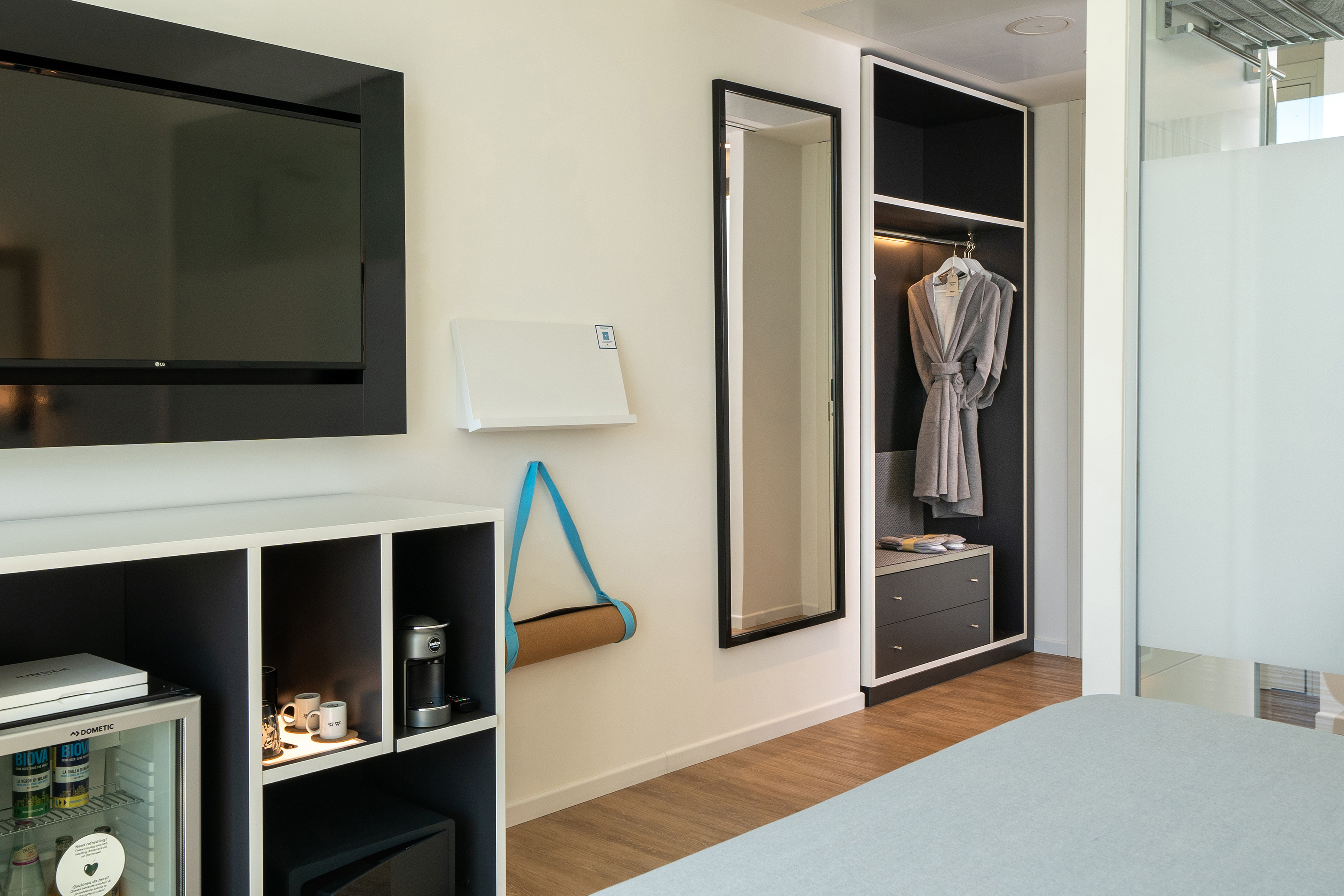 Modern hotel room interior with TV, mini-bar, coffee maker, yoga mat, closet.
