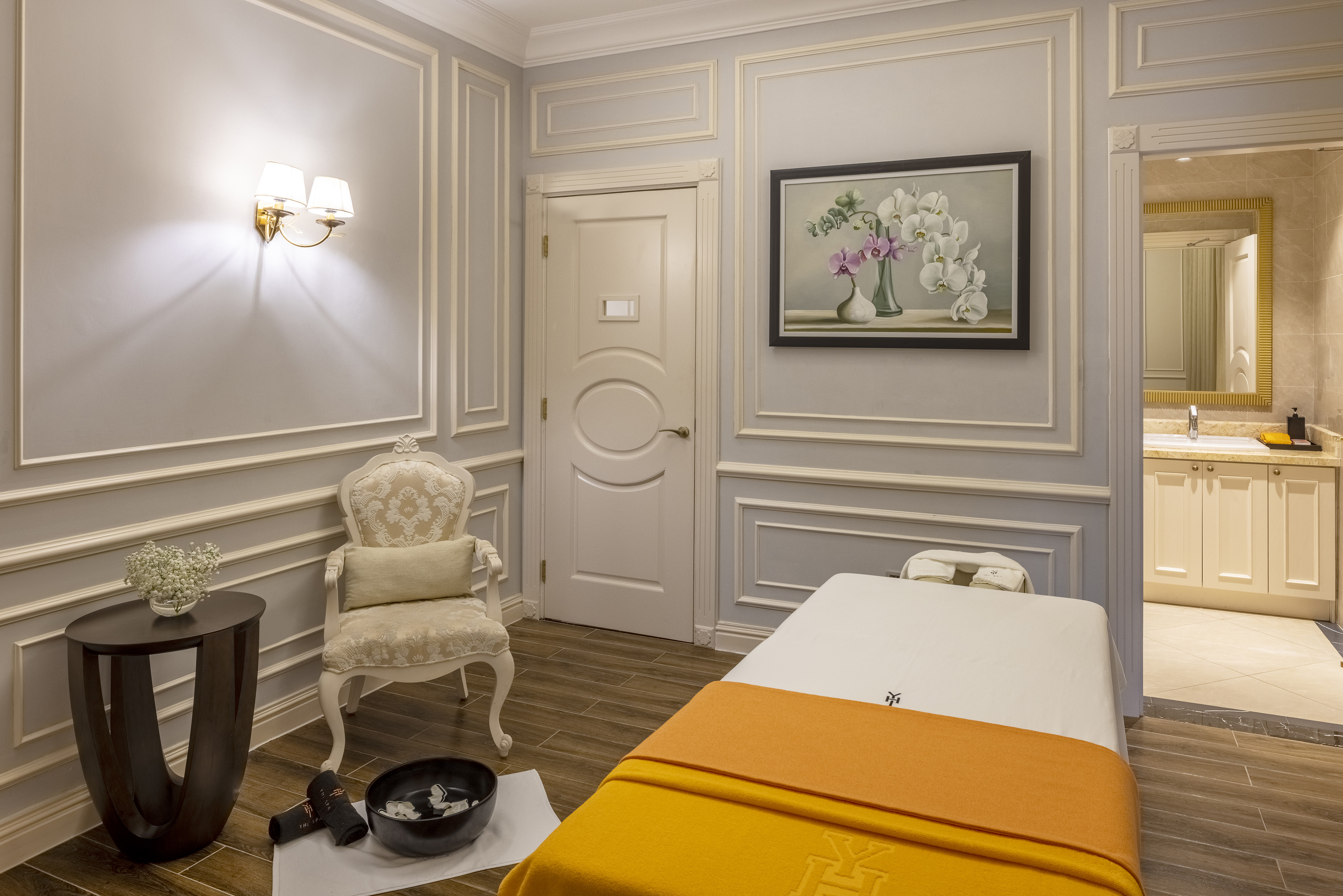 Luxury spa treatment room with massage bed, classic chair, and vanity.