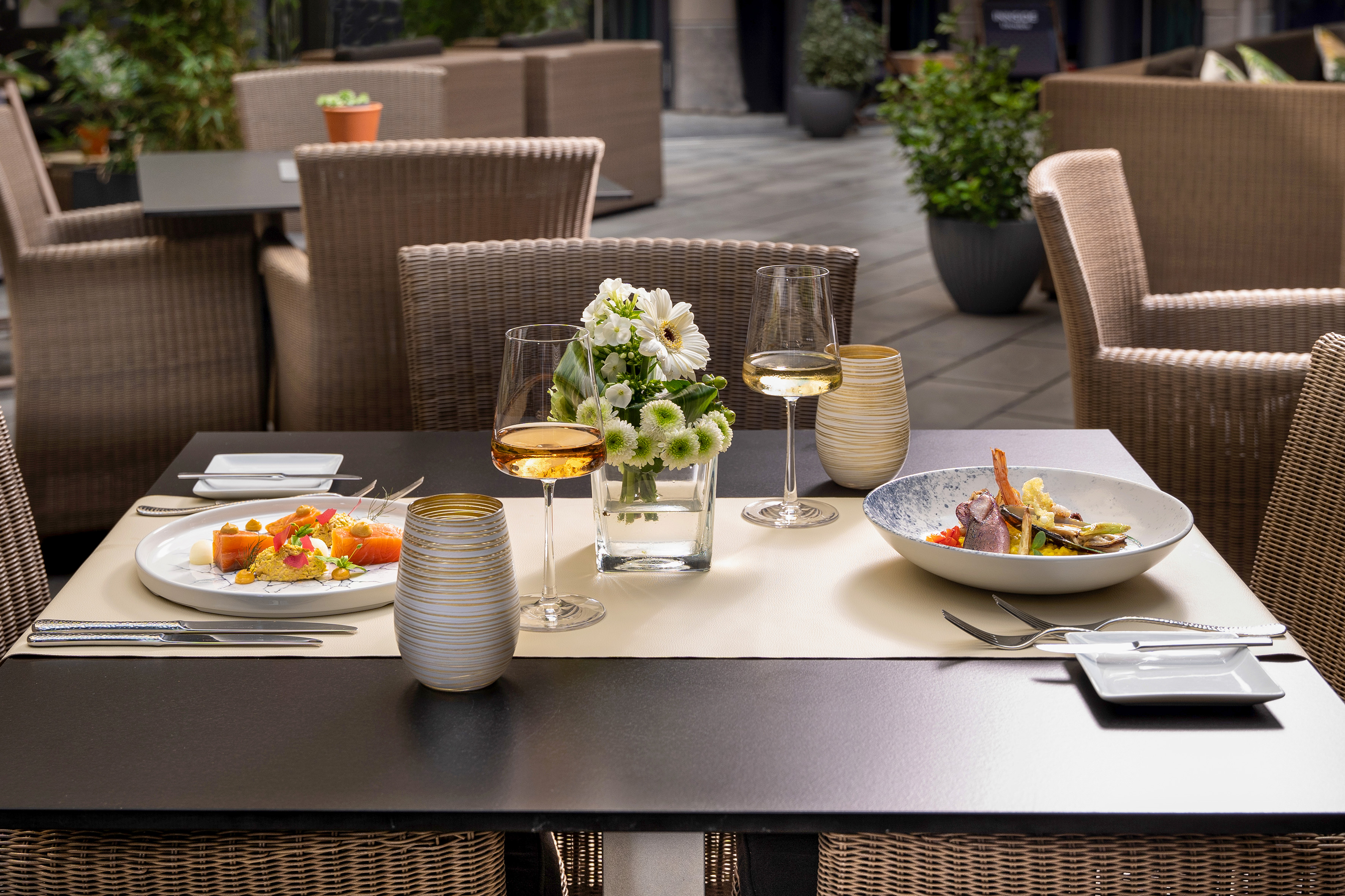 Gourmet food and wine on an outdoor patio dining table with flowers. - VEN Patio - Innside Dresda, Dresda