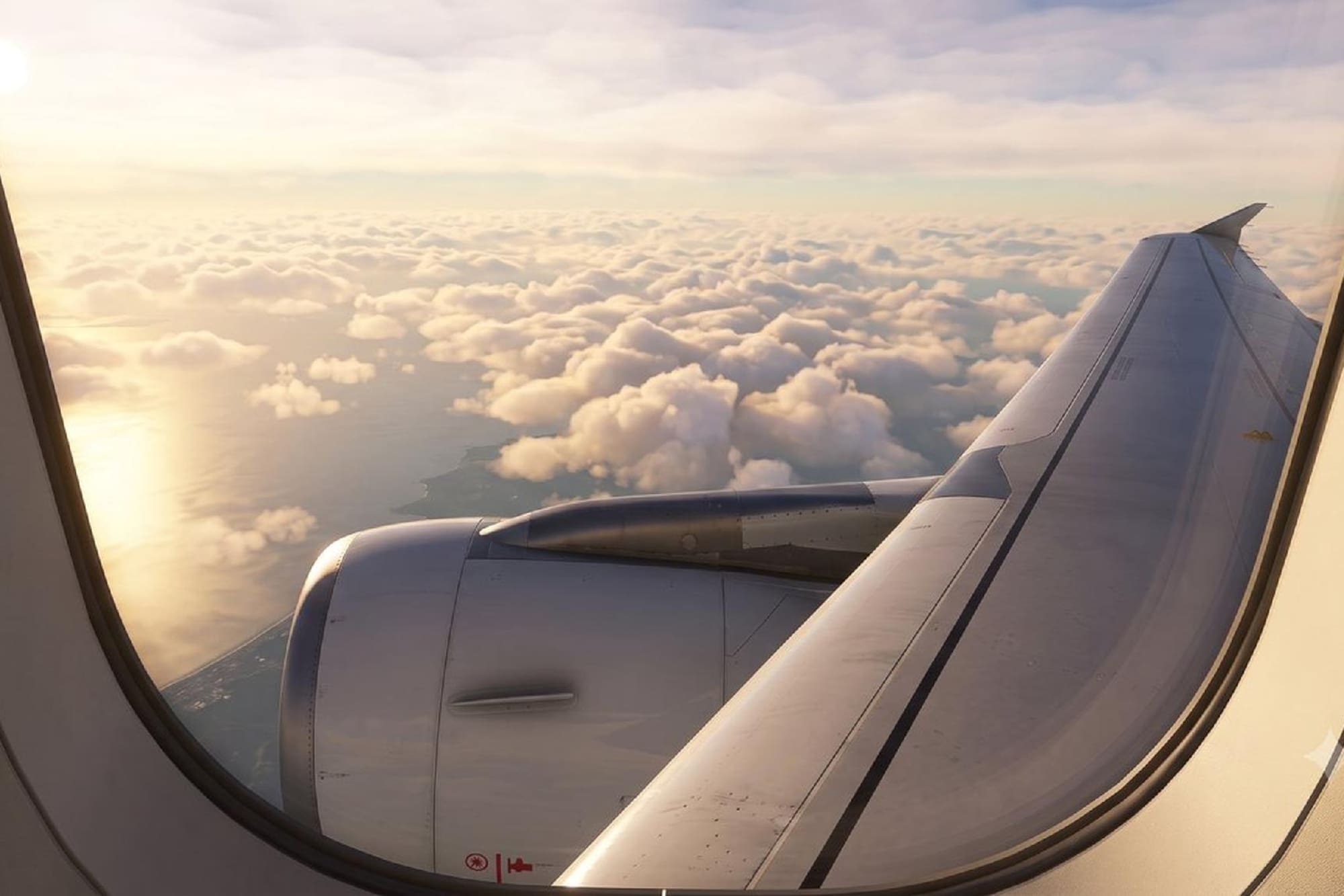 Airplane wing and engine above sunlit clouds and ocean from window. Travel.